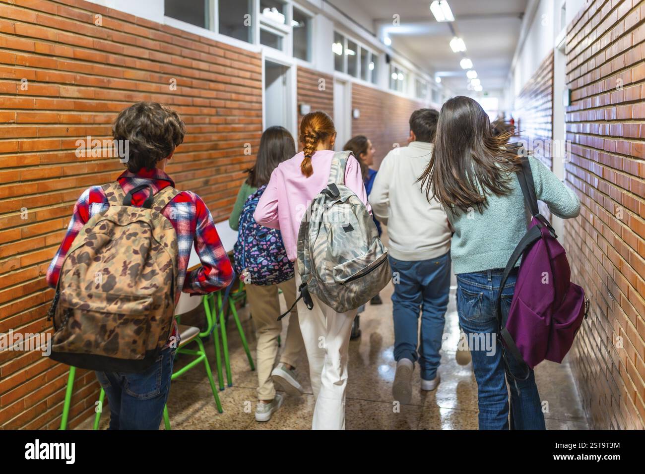 Gruppo di studenti che camminano lungo il corridoio della scuola tra una lezione e l'altra, portano con sé zaini e si precipitano alla lezione successiva Foto Stock