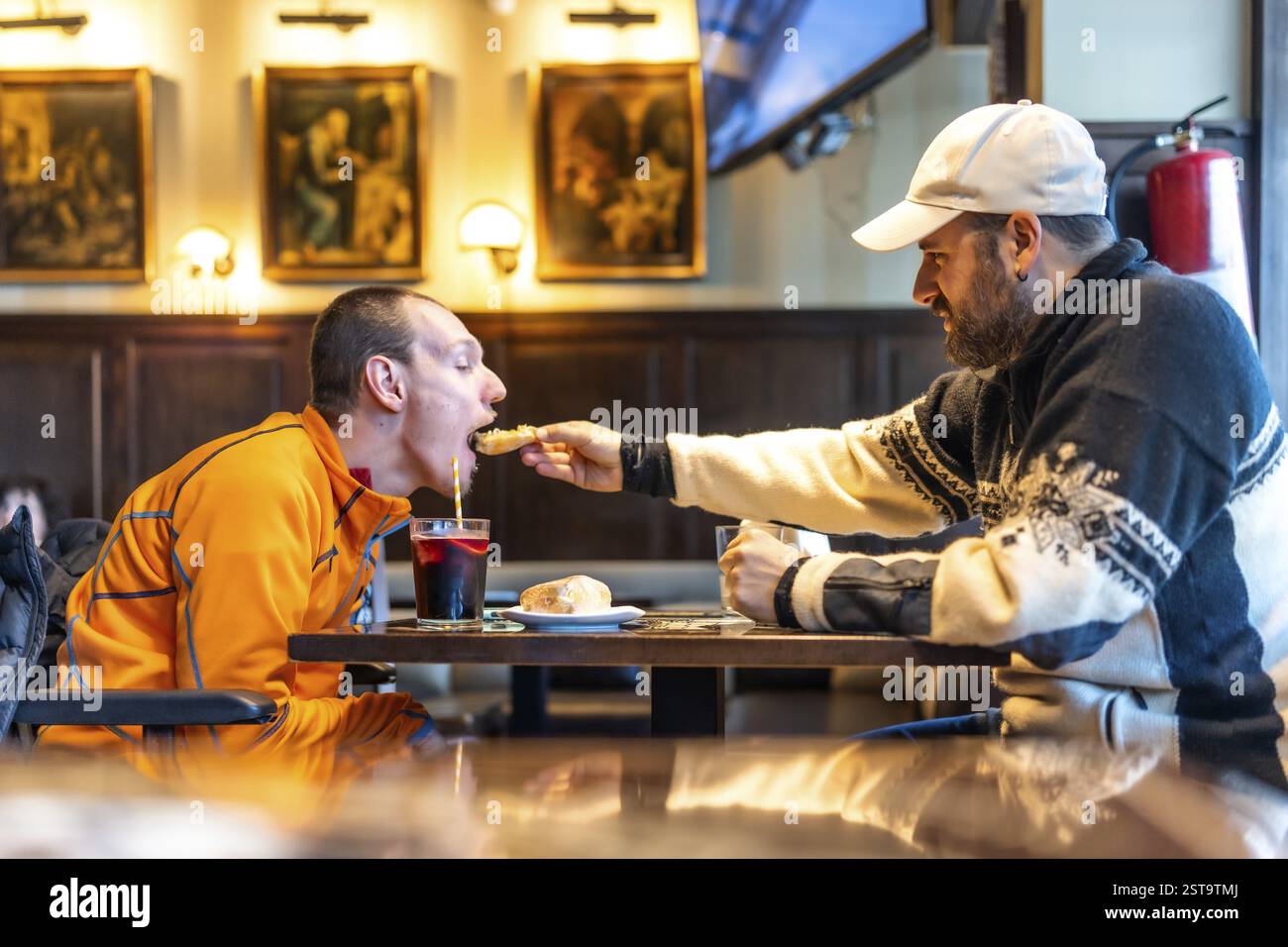 Un momento di grande amicizia aiuta il suo amico disabile a gustare un pasto in un ristorante, sottolineando l'inclusione e il sostegno Foto Stock
