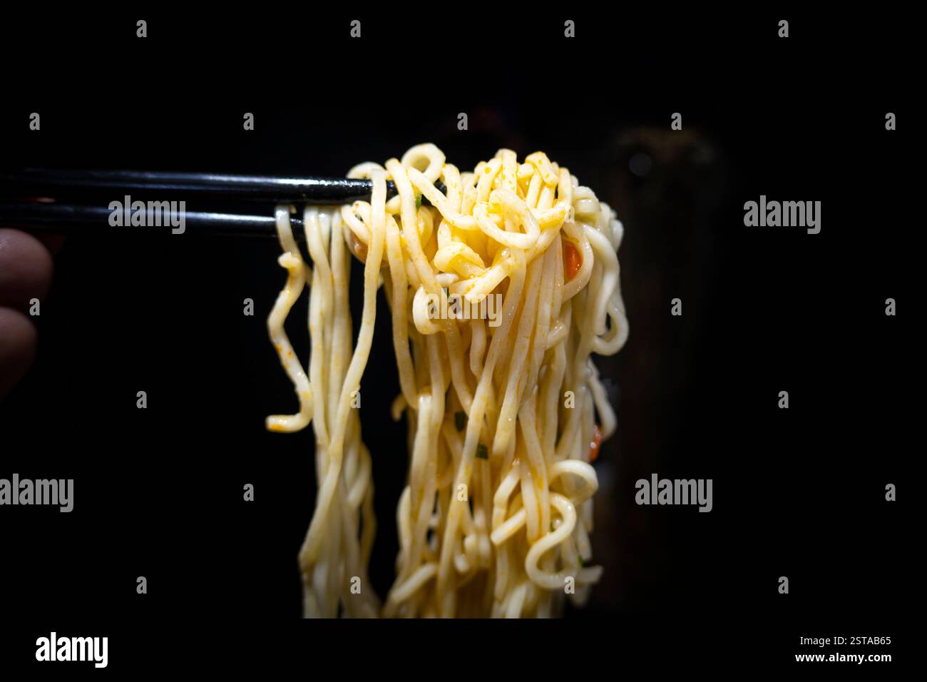 la mano maschile mescola spaghetti istantanei con bacchette in un recipiente su sfondo nero. Foto Stock