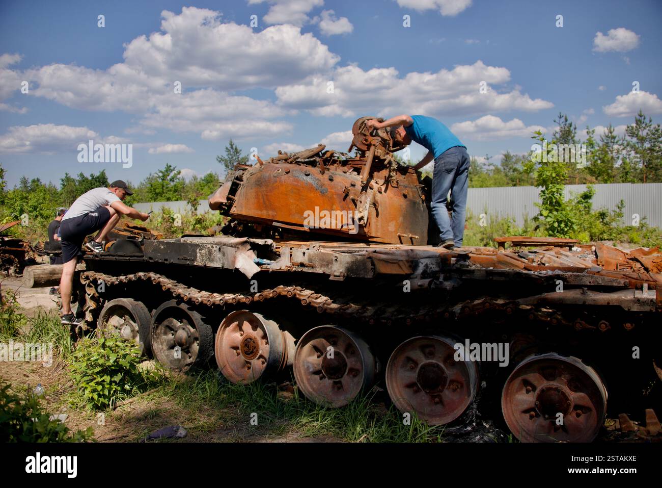 I residenti osservano i veicoli blindati che sono stati raccolti in un cosiddetto cimitero di carri armati vicino a Bucha, Ucraina, l'8 giugno 2022. Foto Stock