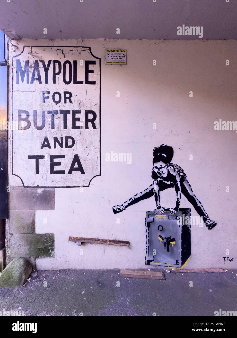 Insegna fantasma per Maypole per il burro e il tè su un muro a Longden Court, accanto a graffiti di una ragazza che salta su una cassaforte. Buxton. Foto Stock