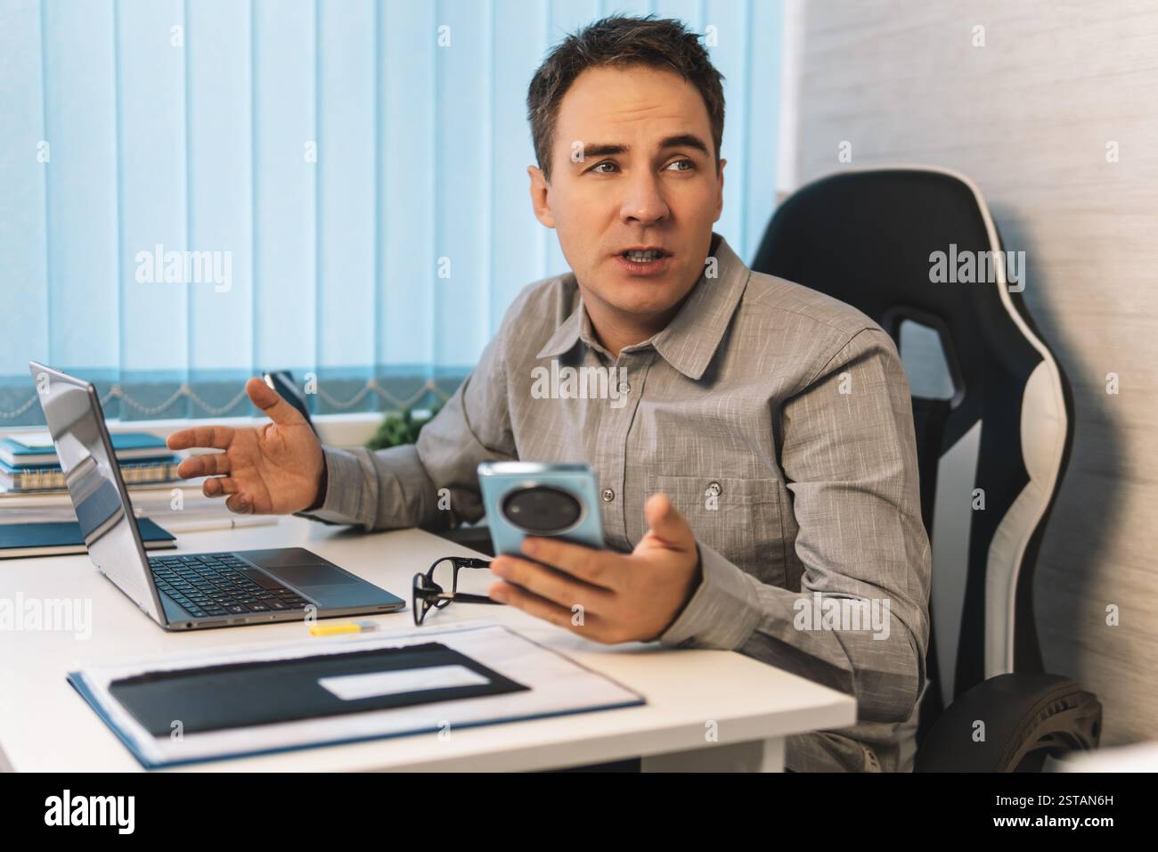 Uomo professionista che lavora su un notebook a una scrivania moderna durante il giorno in un elegante spazio di lavoro. Un uomo d'affari viene distratto dalle conversazioni Foto Stock