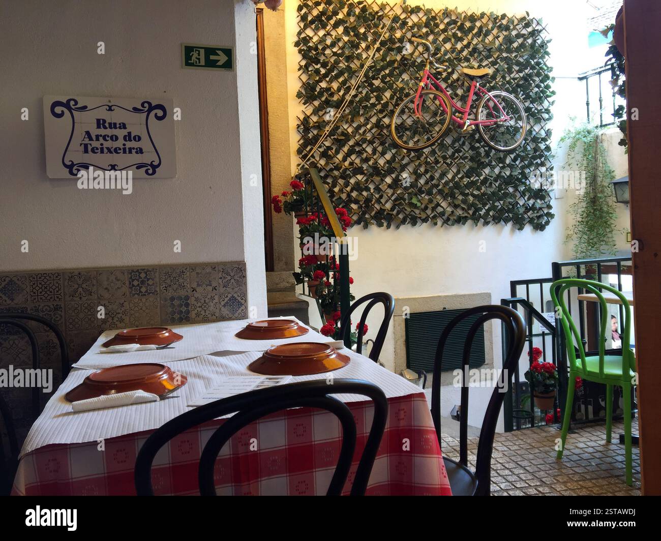 Caffetteria all'aperto a Sintra, Portogallo. La bicicletta rossa è appesa su una parete sopra i tavoli con tovaglie e piatti a scacchi rossi e bianchi. La scala porta a salire Foto Stock