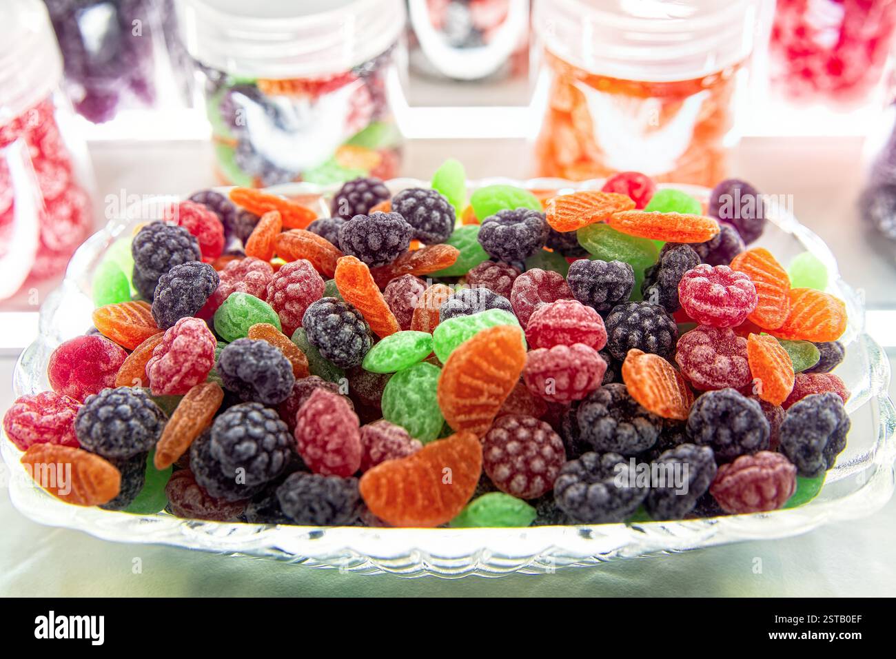 Mucchio di caramelle colorate a forma di frutti di bosco e frutta in un recipiente di vetro. Dolci naturali focalizzati sulla selezione. Foto Stock