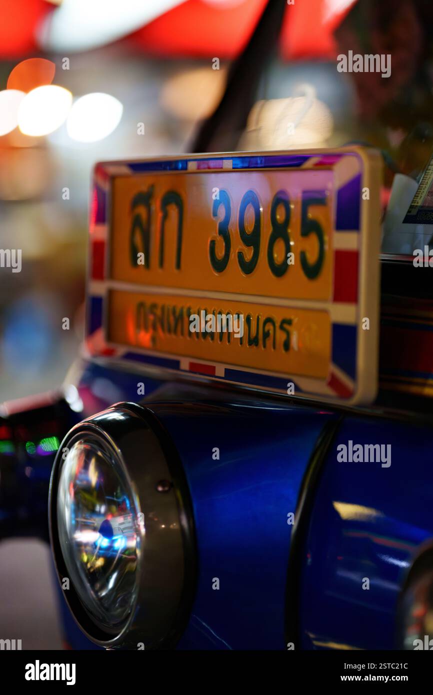 Uno scatto ravvicinato della targa di un tuk-tuk a Bangkok, con caratteri e numeri thailandesi. Il vivace colore blu del tuk-tuk e del ligh sfocato Foto Stock