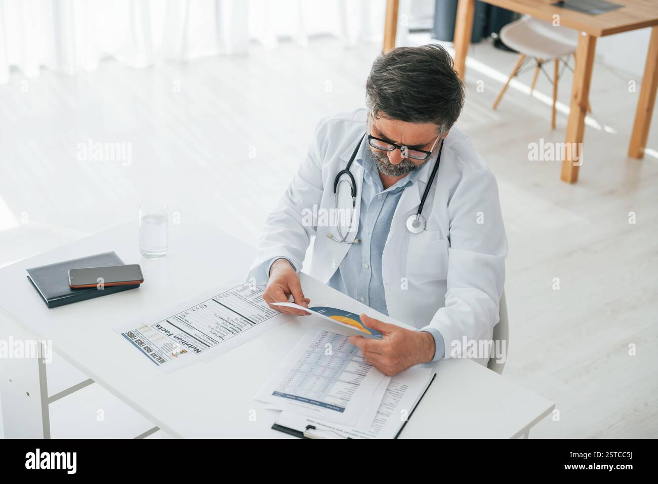 L'uomo sta lavorando con i documenti. Un medico maturo in giacca bianca è in ufficio. Foto Stock