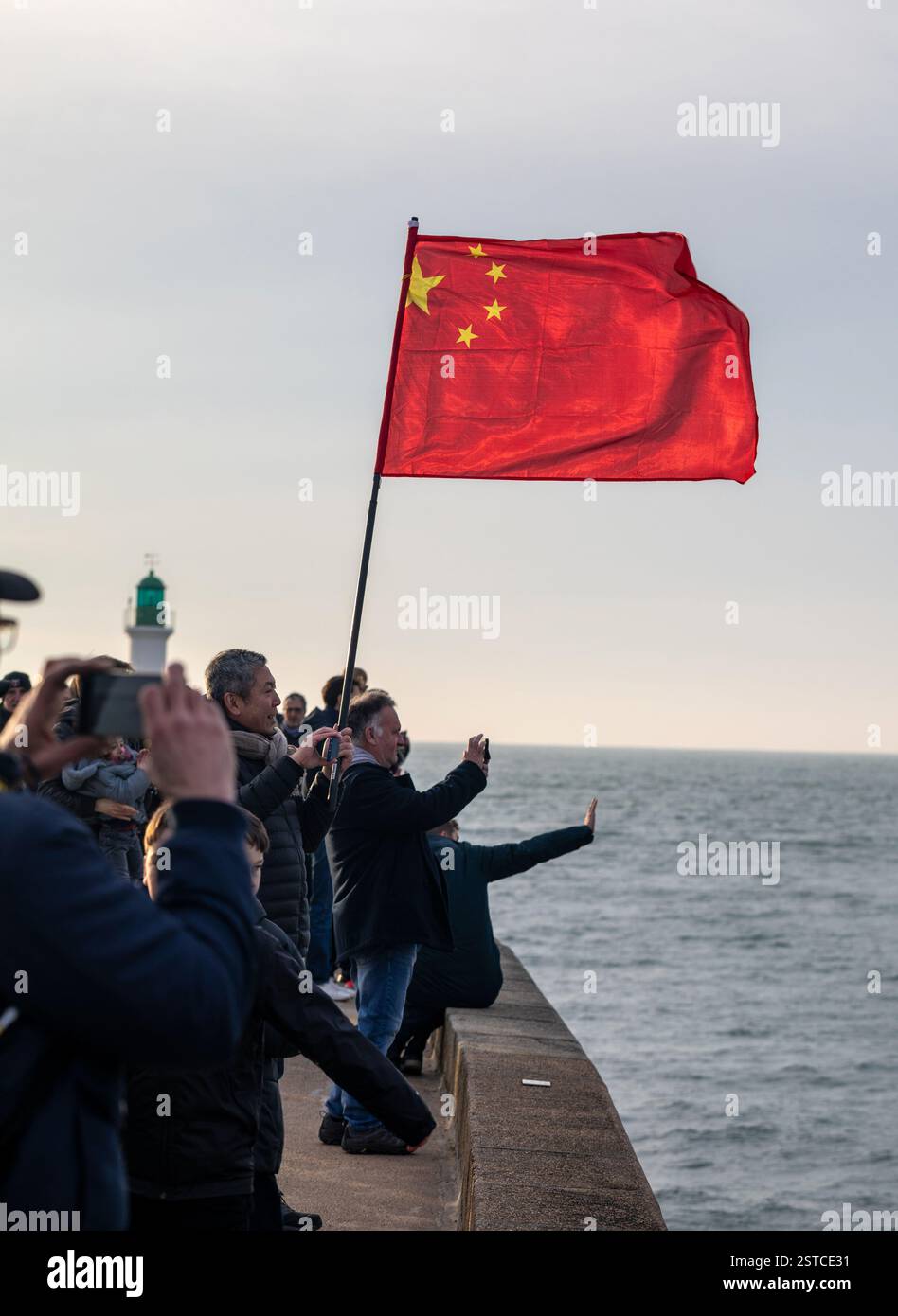 Sostenitori con la bandiera cinese per l'arrivo dello skipper Jingkun Xu per il Vendee Globe 2024 il 18 febbraio 2025. A Les Sables d'Olonne, Francia. Foto Stock