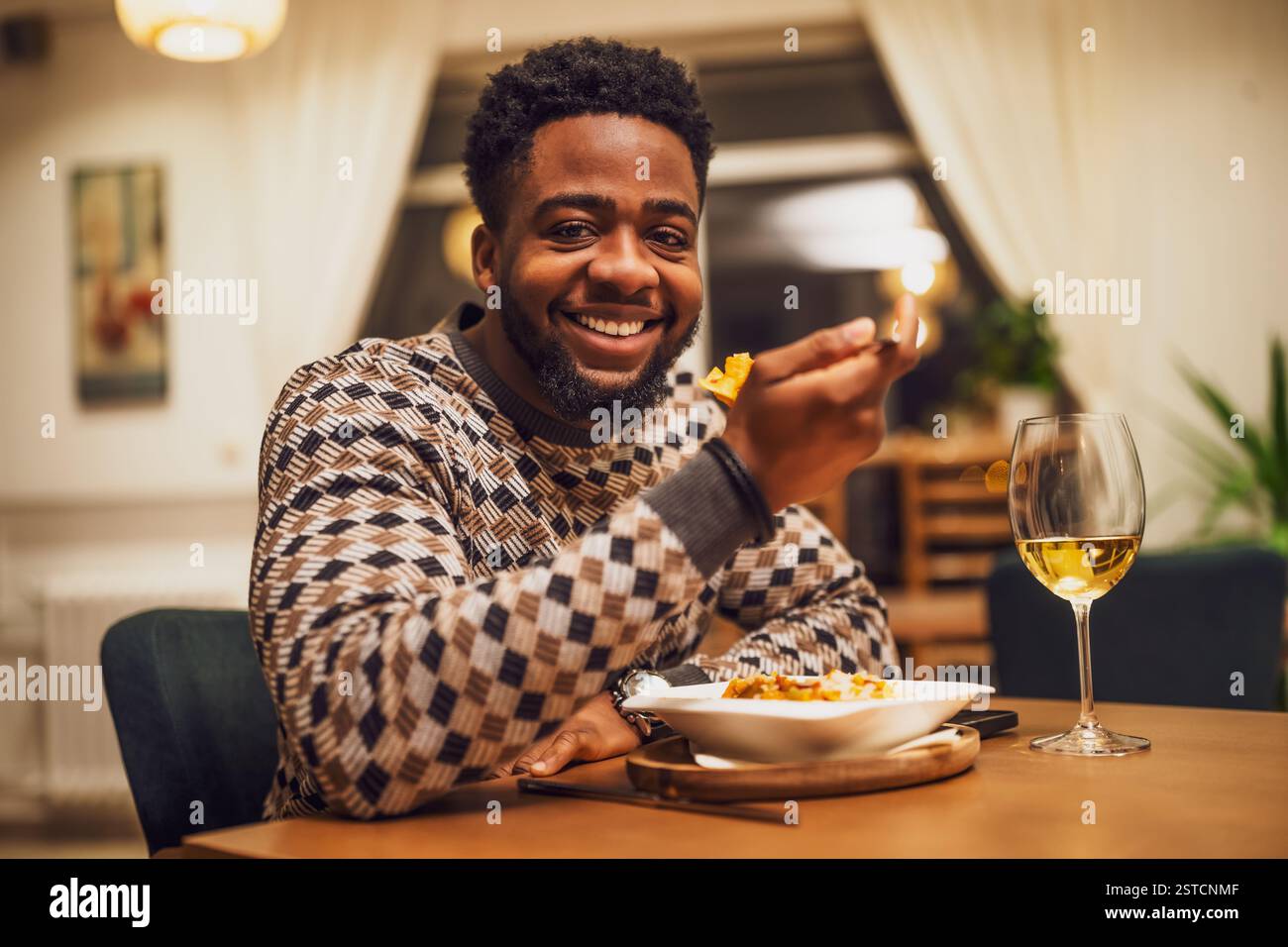 Il giovane uomo nero felice sta cenando e mangiando vino al ristorante. Guarda la telecamera e sorride. Foto Stock