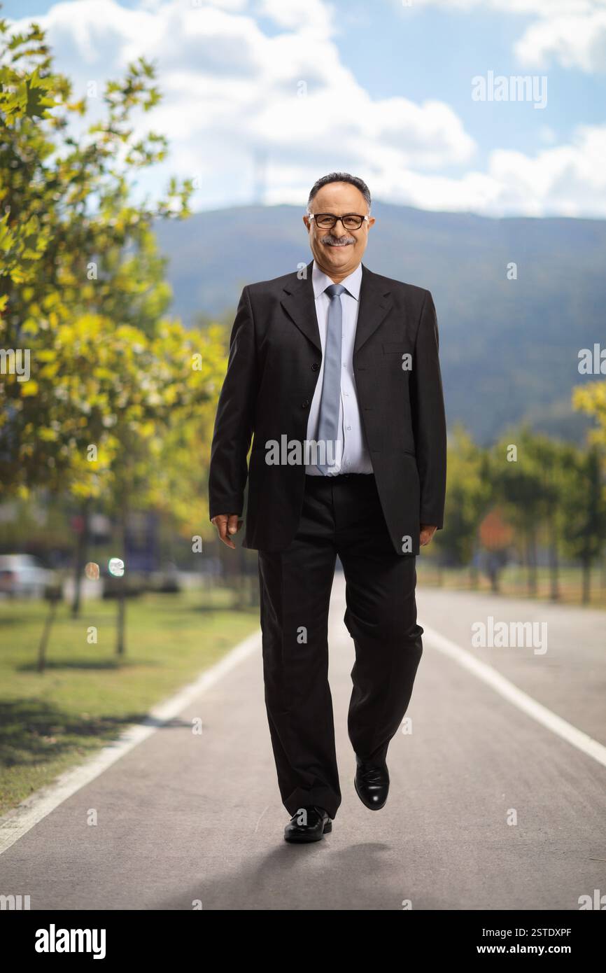 Ritratto completo di un uomo d'affari maturo che sorride e cammina in un parco Foto Stock