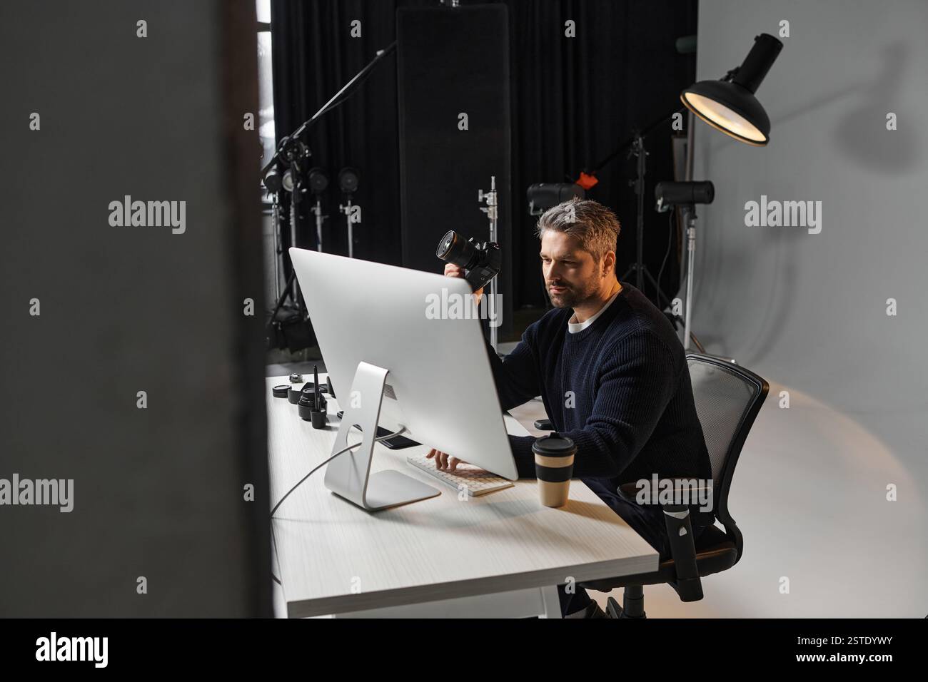 Un lavoratore esperto si concentra sull'editing di contenuti digitali mentre si gusta una bevanda calda alla scrivania. Foto Stock