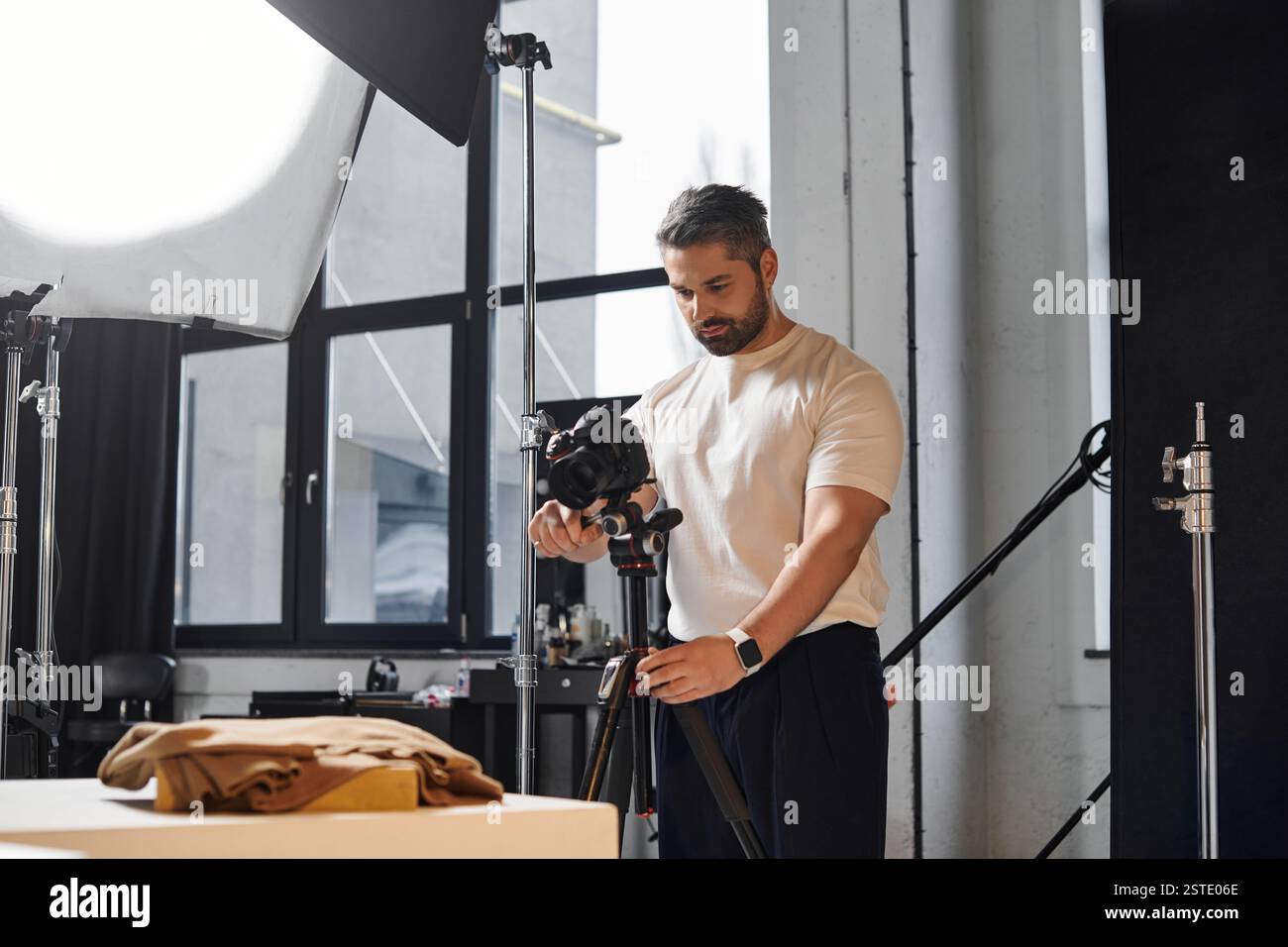 Con un intento mirato, un uomo prepara la sua macchina fotografica in uno spazio luminoso dello studio. Foto Stock