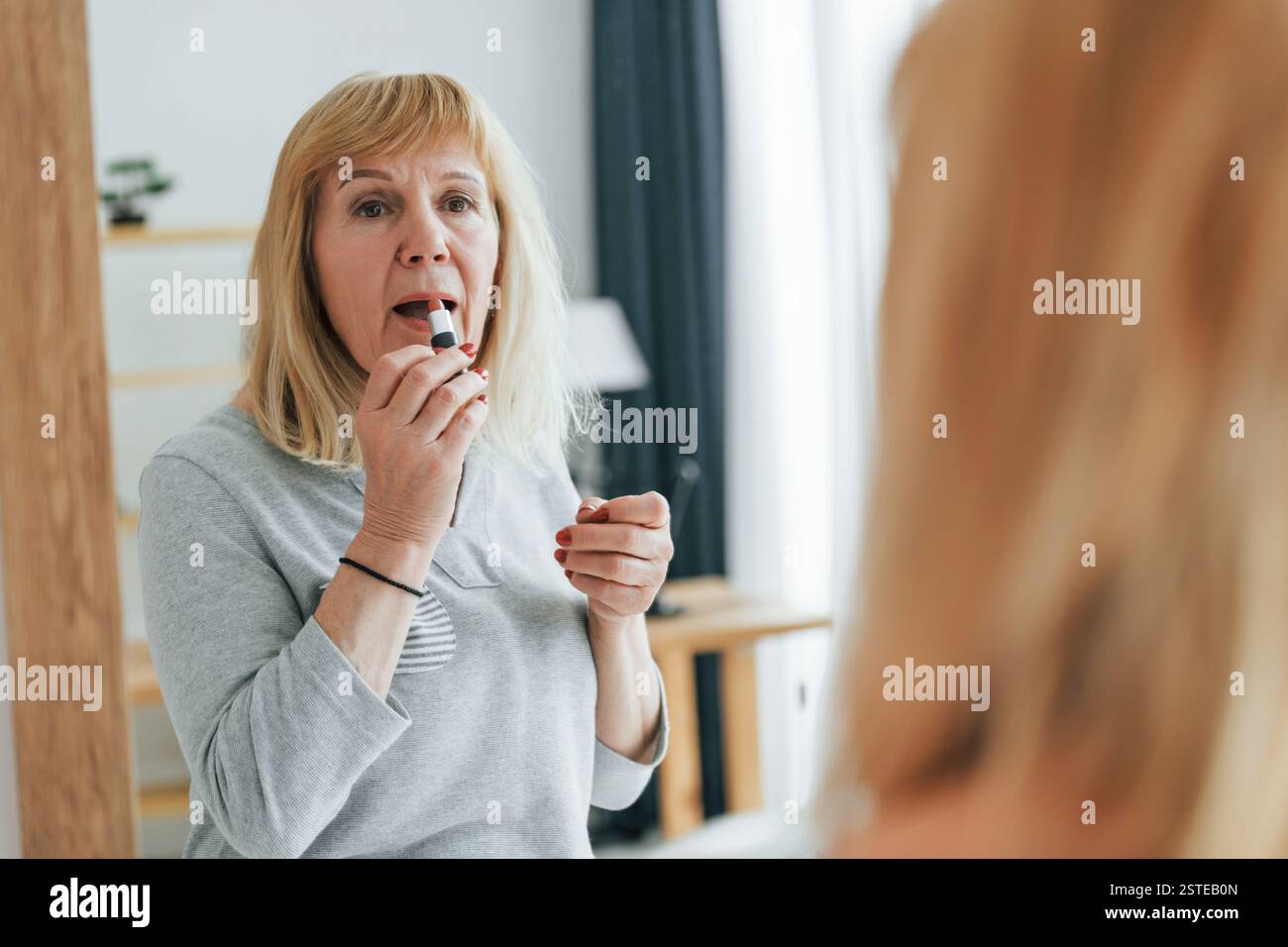 Guarda lo specchio, cura di sé. Una donna anziana con i capelli rossi è a casa da sola. Foto Stock