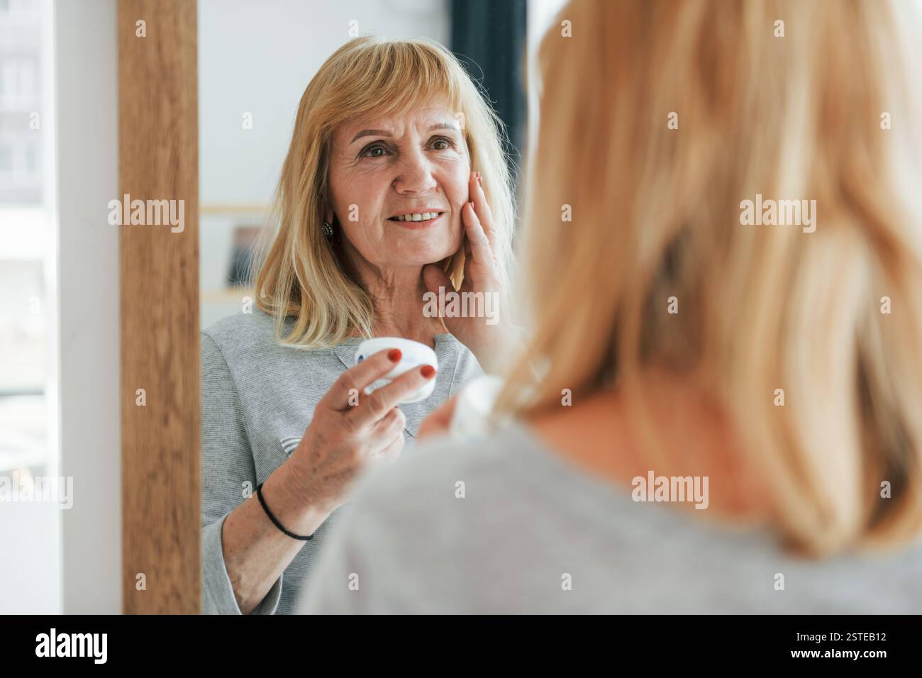 Guarda lo specchio, cura di sé. Una donna anziana con i capelli rossi è a casa da sola. Foto Stock