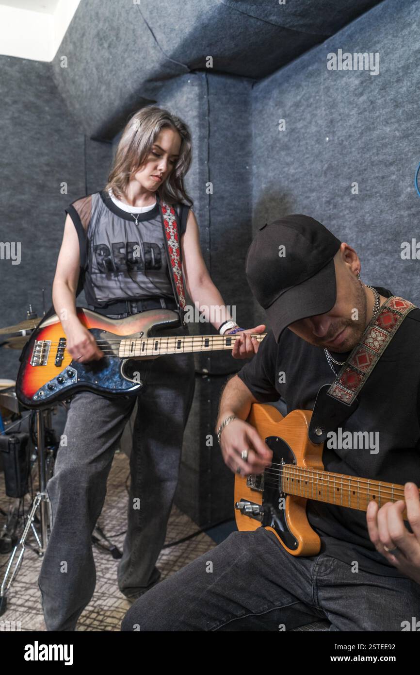 Bassista femminile e chitarrista elettrica che suonano insieme in uno studio di prova insonorizzato professionale. I membri della rock band praticano spettacoli dal vivo e arrangiamenti musicali. Foto Stock