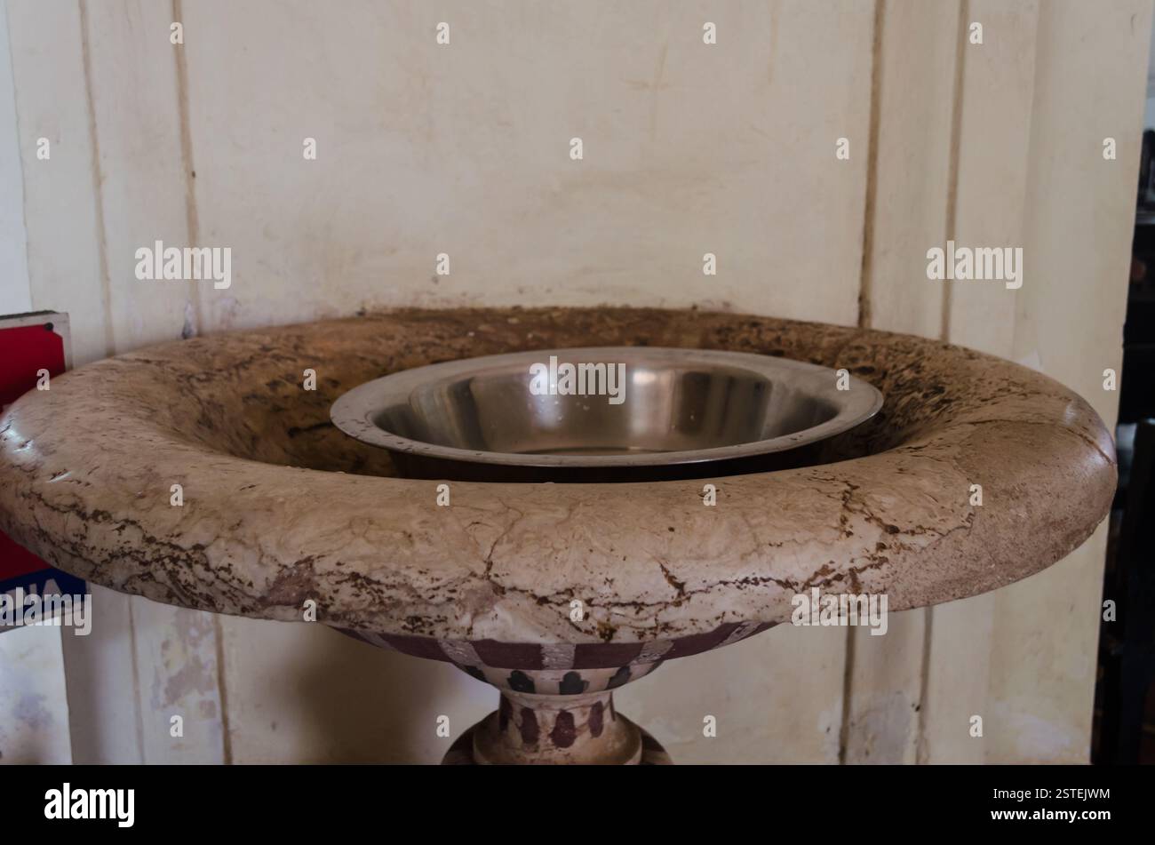 Vista ravvicinata di un antico fonte battesimale in pietra intagliata con una vasca in metallo all'interno di una chiesa storica a Old Goa, India. Foto Stock
