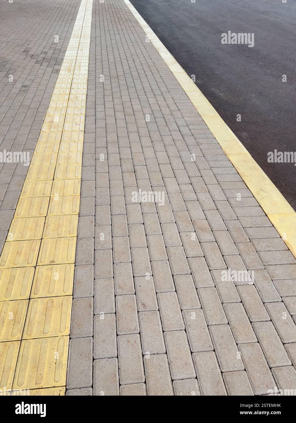 vista di un marciapiede a motivi geometrici con linee guida gialle che mostrano un ambiente urbano con pavimentazione tattile. Foto Stock