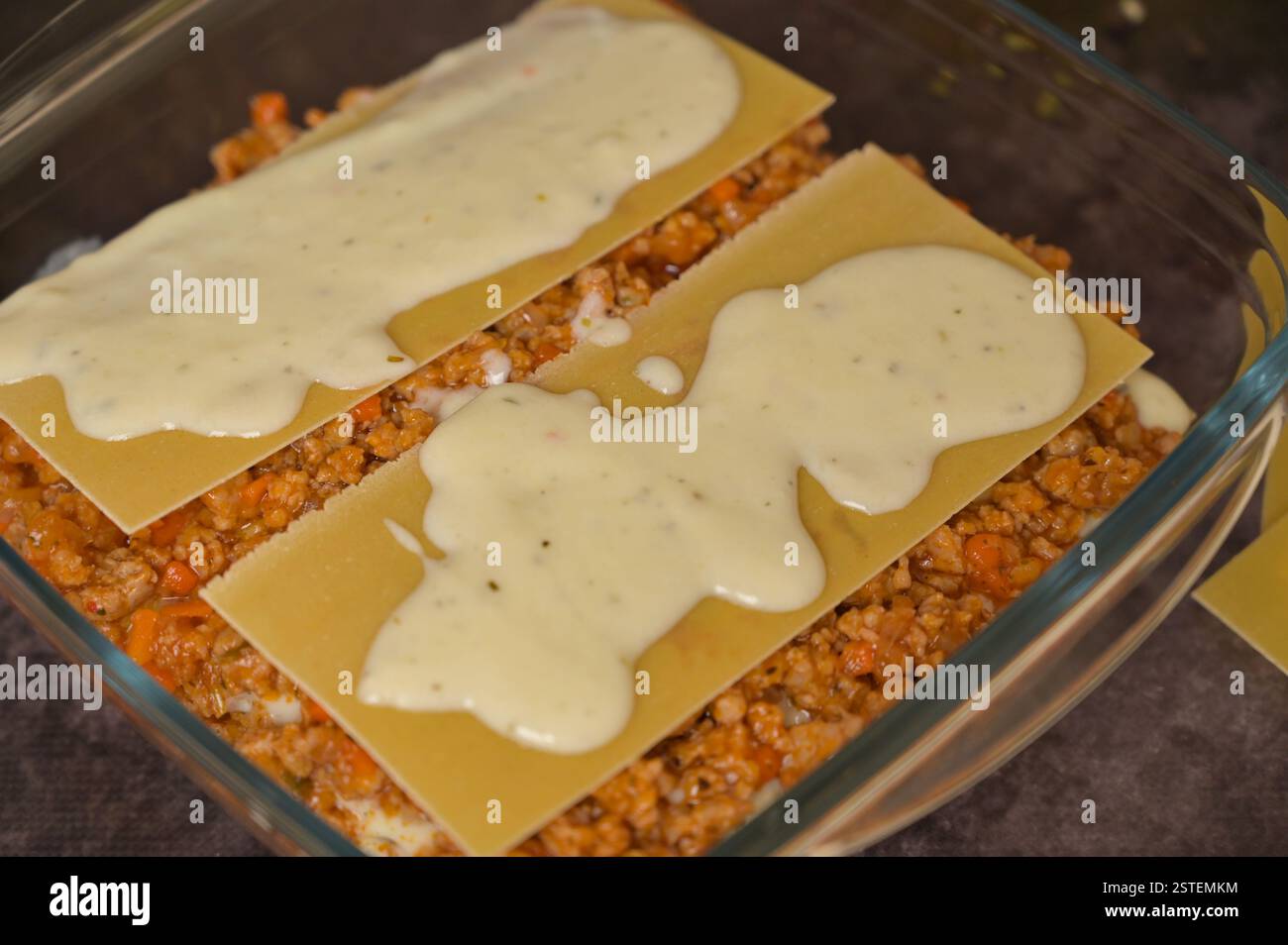 Primo piano. Preparazione per la cottura delle lasagne fatte in casa. Lastre di pasta di lasagne, bolognese e béchamel in forma di bicchiere. Sfondo nero Foto Stock