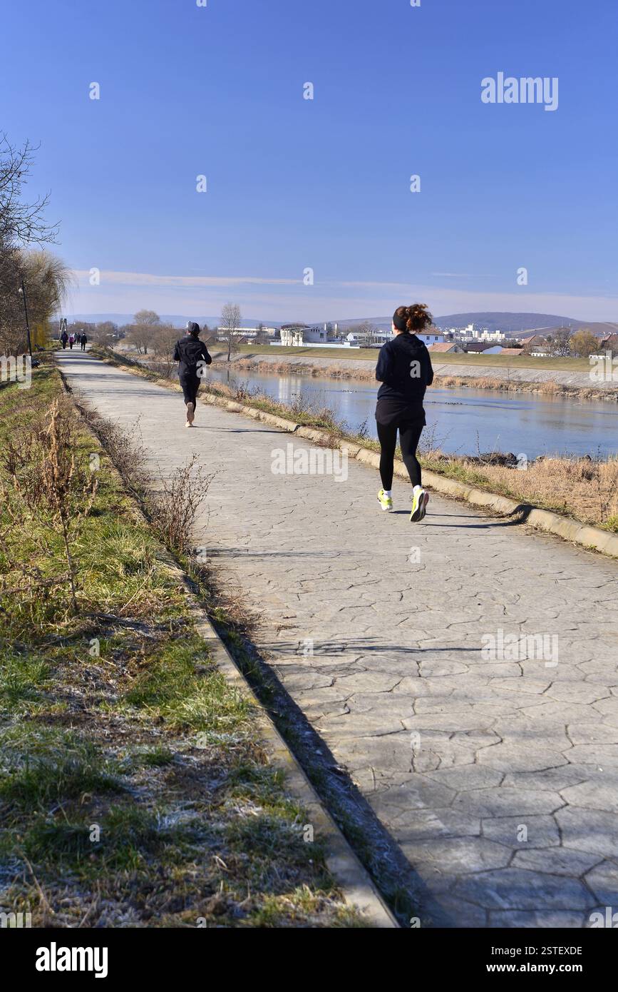 Due giovani donne in primo piano che corrono sulle rive del fiume Mures in una fredda mattina di febbraio Foto Stock