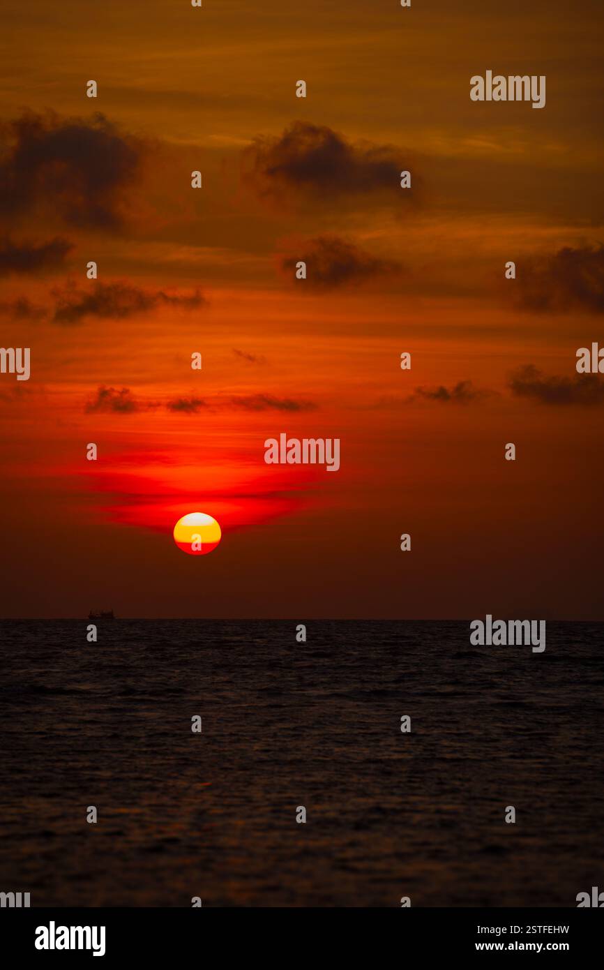 Red Ball of the Sun che scende verso l'orizzonte al tramonto Foto Stock