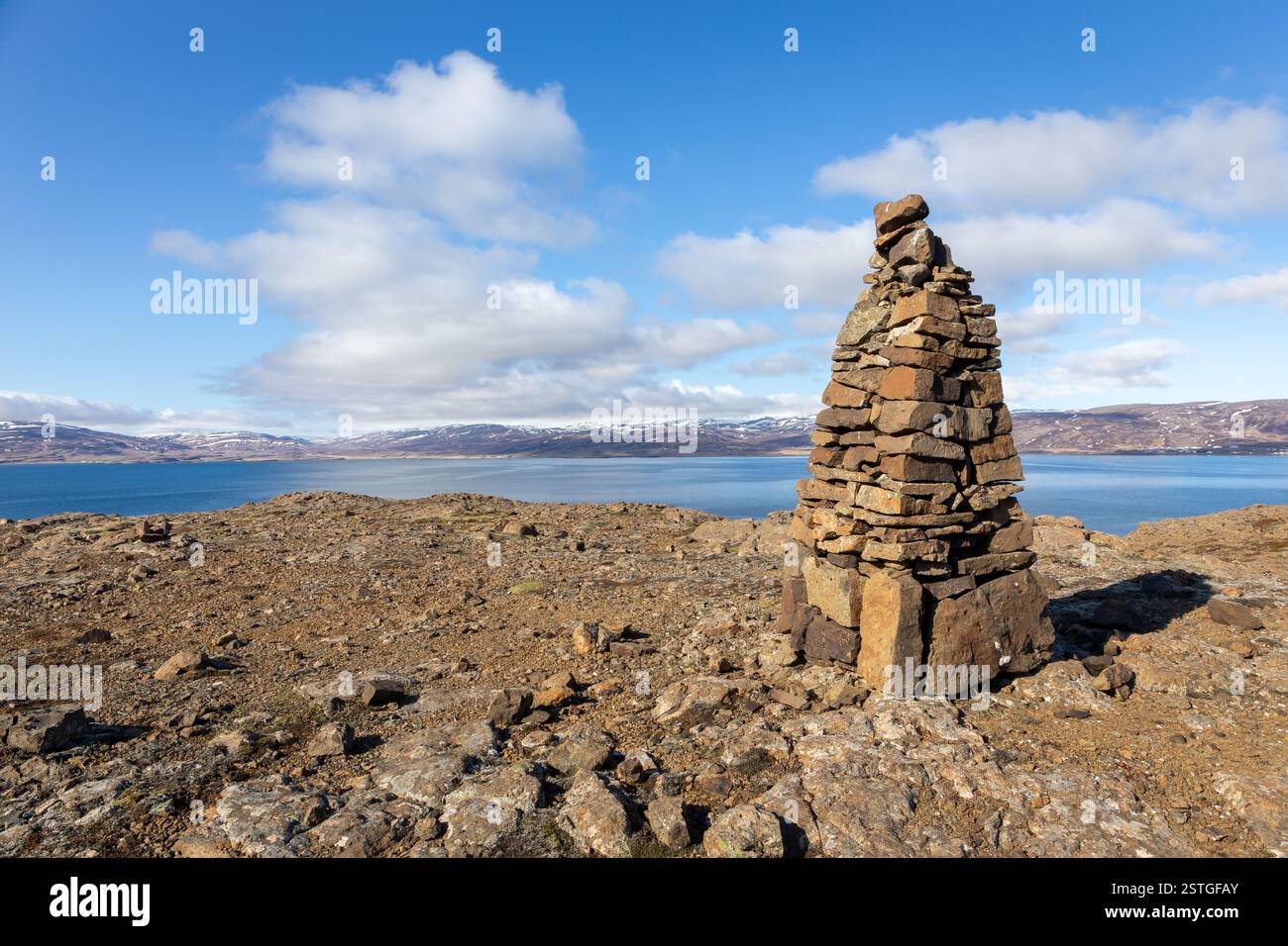 Cairn, un mucchio di pietre fatte dall'uomo che fa il percorso a Westfjords, Islanda, con vista sul mare e montagne innevate sullo sfondo. Foto Stock