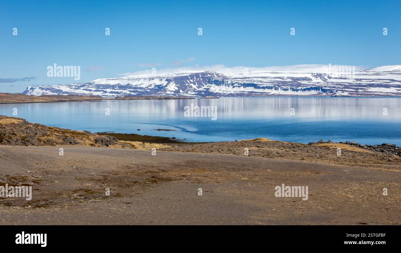 Paesaggio costiero di Westfjords in Islanda con acque cristalline, montagne innevate e cielo blu. Foto Stock