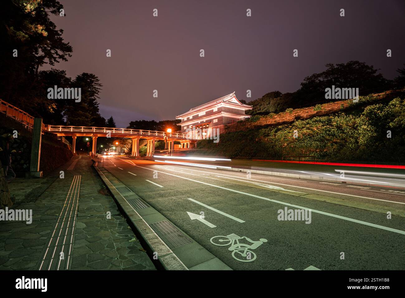 Un cancello storico splendidamente illuminato a Kanazawa, Giappone, catturato di notte con sentieri leggeri dai veicoli di passaggio. Foto Stock