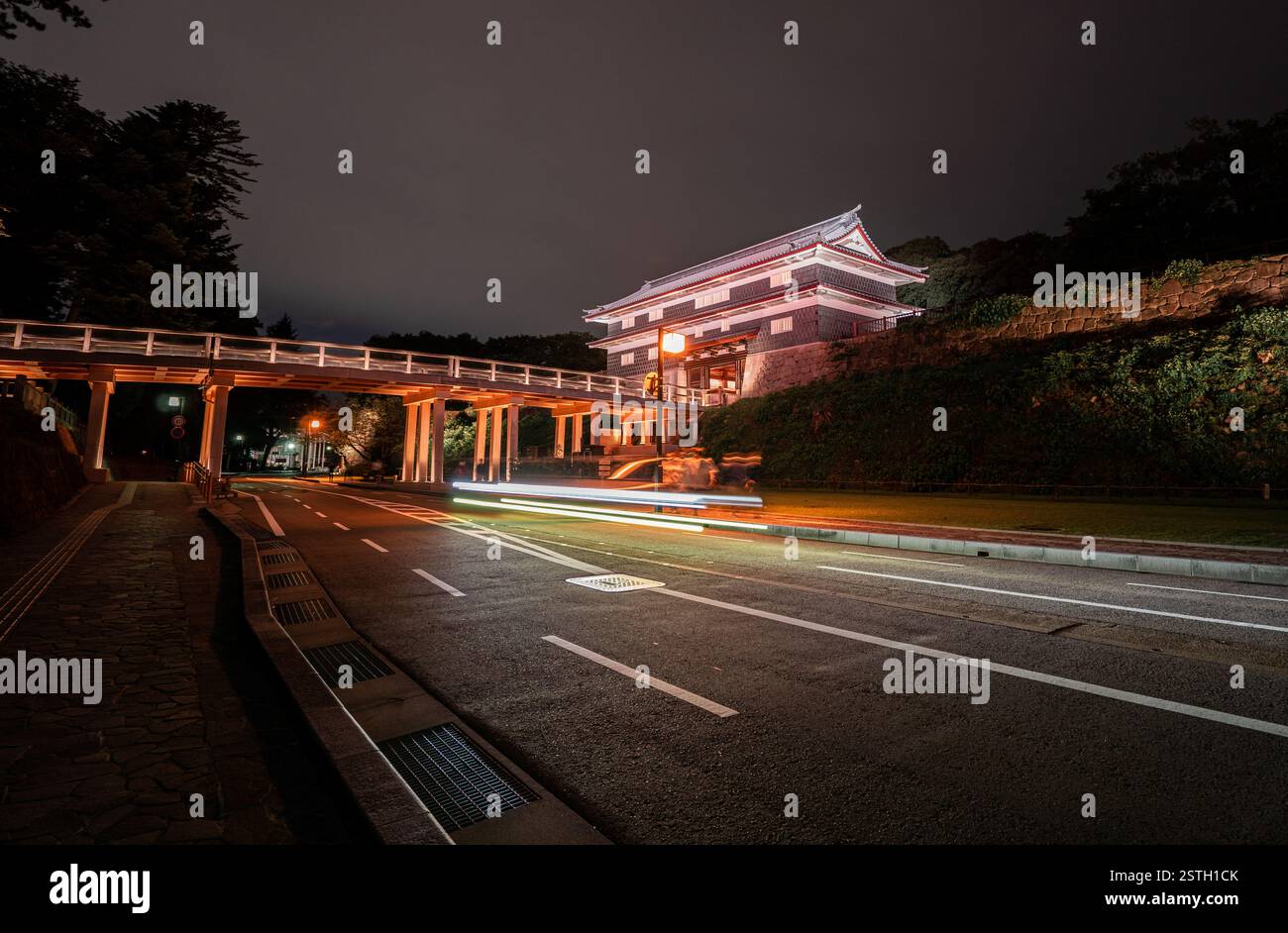 Un cancello storico splendidamente illuminato a Kanazawa, Giappone, catturato di notte con sentieri leggeri dai veicoli di passaggio. Foto Stock