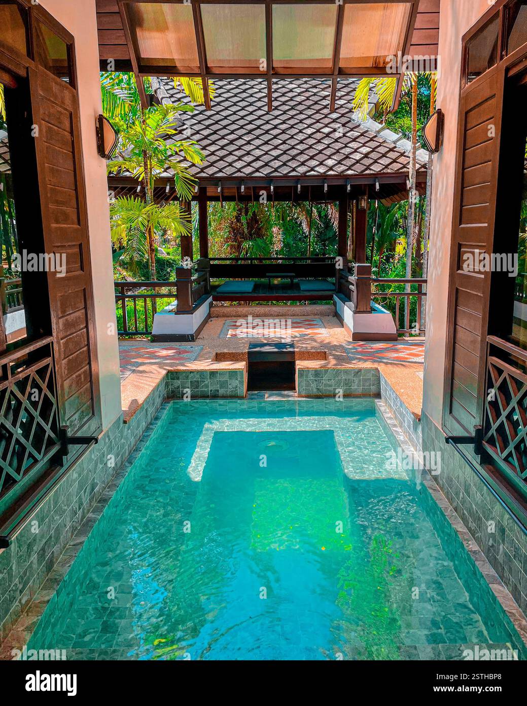 Piscina privata con Padiglione tropicale, piscina a mosaico verde circondata da una villa in stile asiatico con un padiglione ombreggiato sullo sfondo. Foto Stock