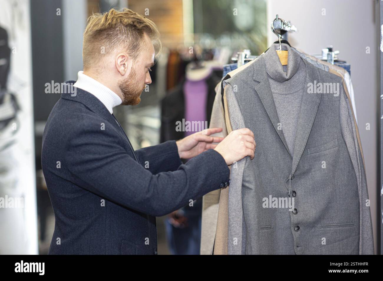 Uomo che sceglie un blazer grigio da una scaffale di vestiti in un negozio Foto Stock
