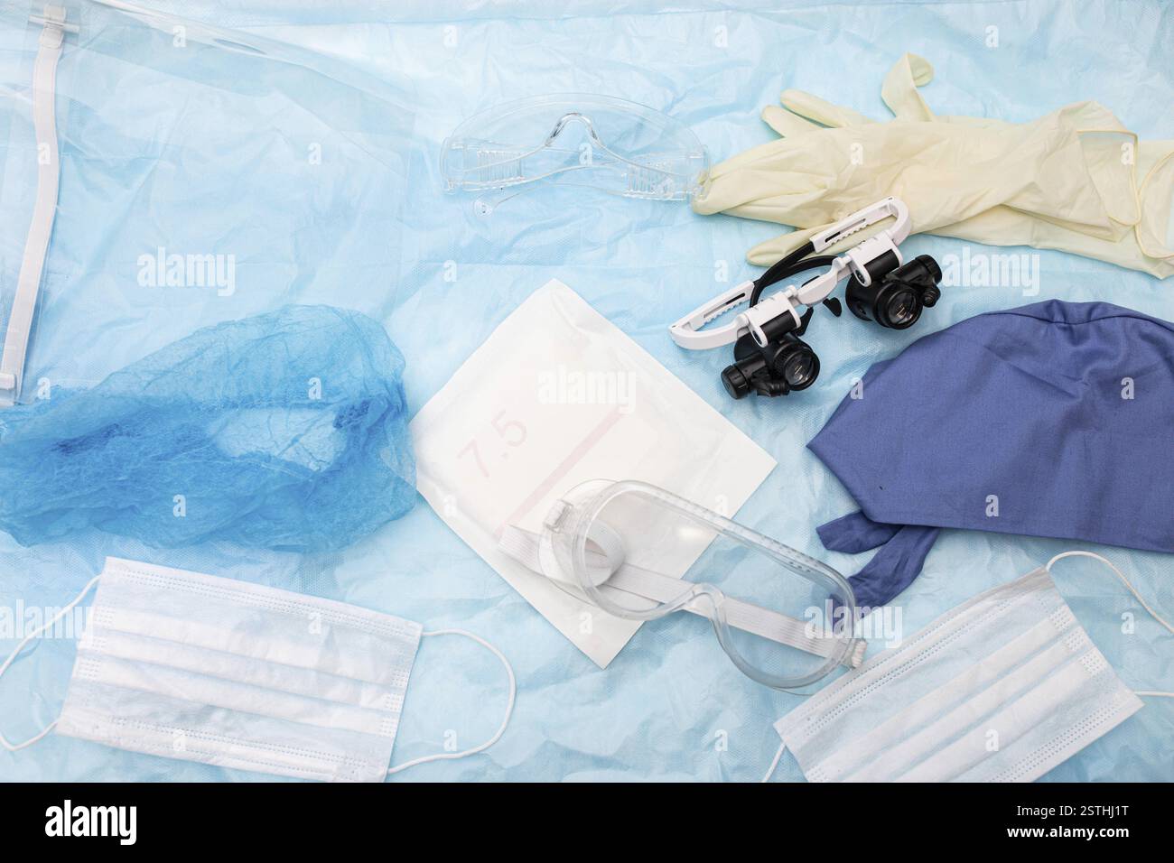 Mix di dispositivi di protezione medica come maschere, cappucci e occhiali di protezione su una superficie blu Foto Stock