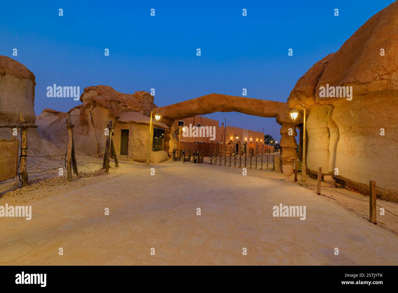 Strada illuminata e arco che conducono agli edifici tradizionali delle grotte rocciose di montagna di Jabal al Qarah di notte nell'oasi di al Ahsa, Arabia Saudita Foto Stock