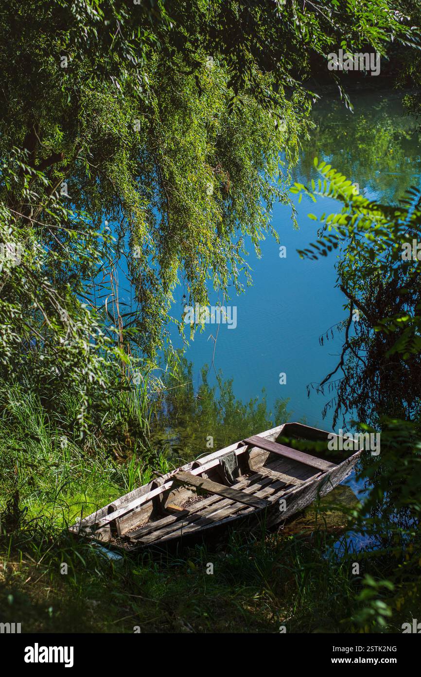 Vecchia barca di legno sulla riva del fiume all'ombra degli alberi Foto Stock