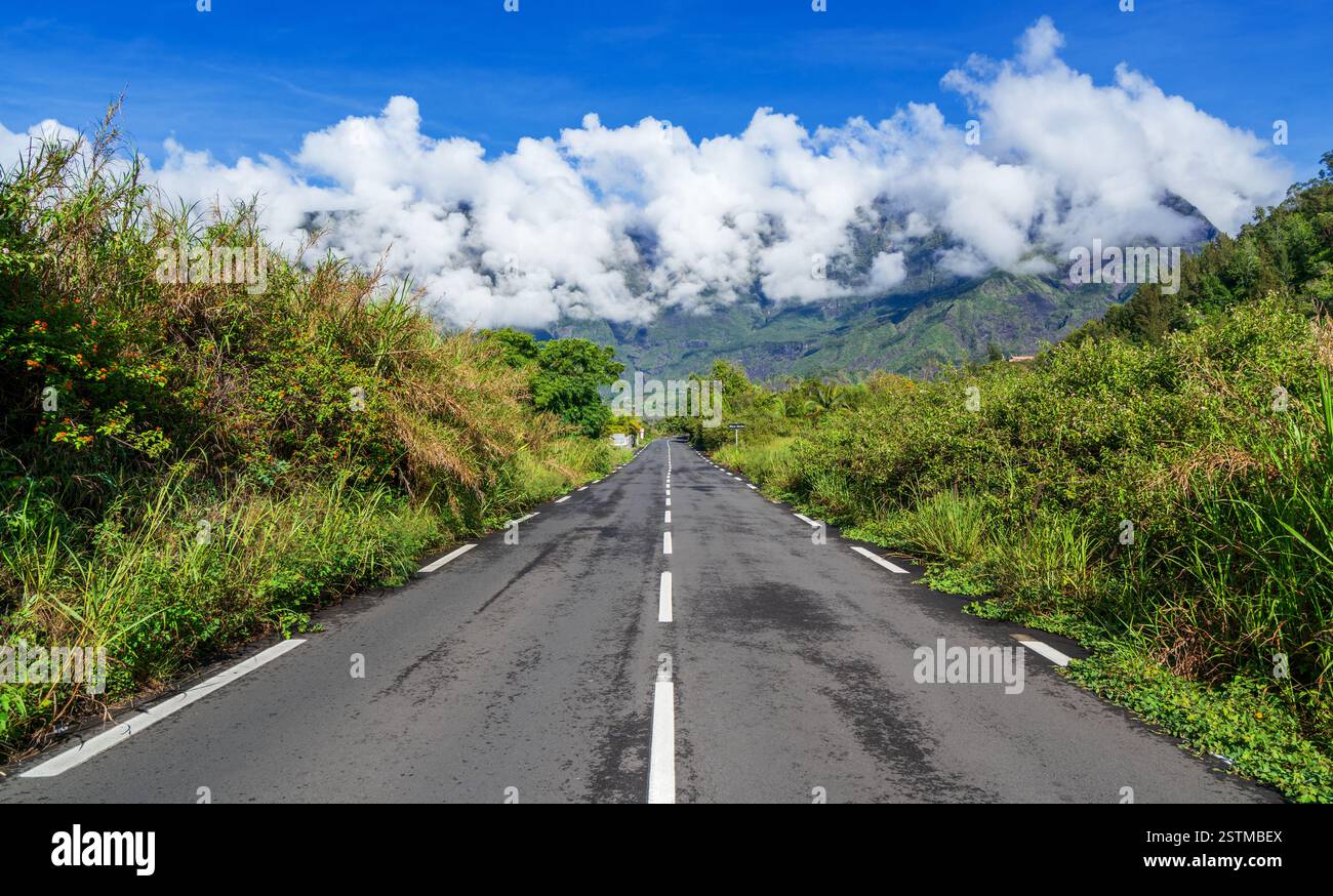 Strada panoramica che conduce a Mare a Seche, Reunion, circondata da vegetazione lussureggiante, spettacolari nuvole e torreggianti montagne in un paradiso tropicale Foto Stock Strada panoramica che conduce a Mare a Seche, Reunion, circondata da vegetazione lussureggiante, spettacolari nuvole e torreggianti montagne in un paradiso tropicale Foto Stock