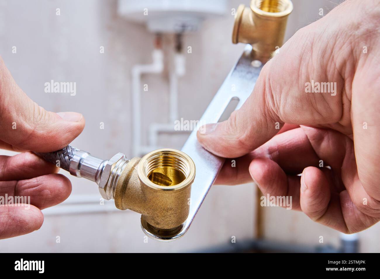 Il tubo dell'acqua flessibile intrecciato viene collegato manualmente a un raccordo idraulico in ottone, fissando il sistema di alimentazione dell'acqua. Foto Stock