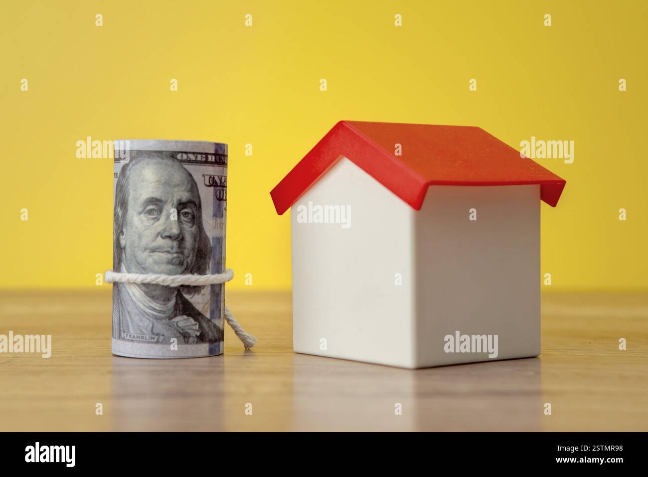 Una casa dei giocattoli con un mucchio di banconote in dollari. Proprietà di abitazioni, immobili e pianificazione finanziaria. Copia spazio per il testo. Foto Stock