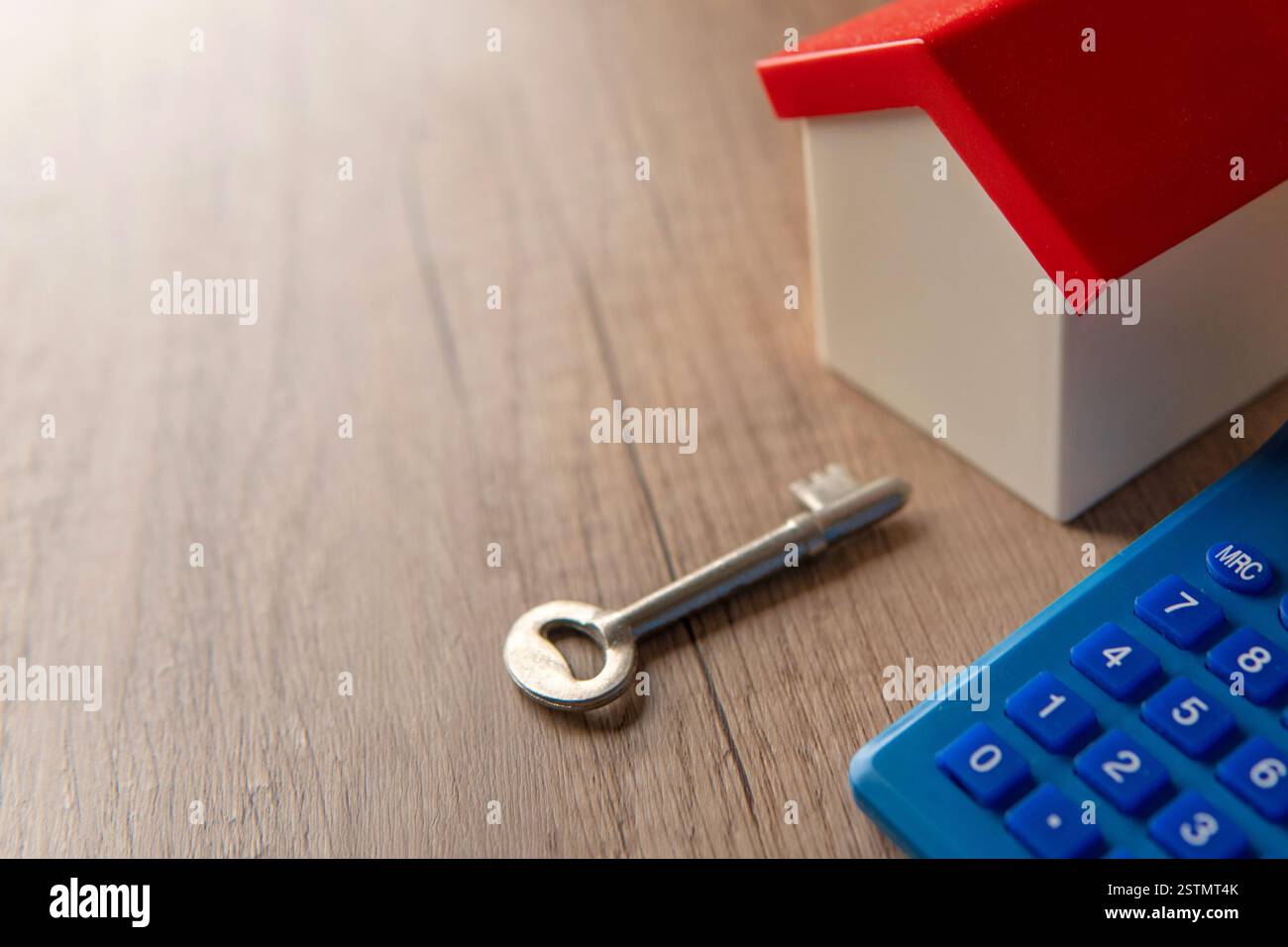 Una casa dei giocattoli, una chiave e una calcolatrice su un tavolo di legno. Proprietà di abitazioni, immobili e pianificazione finanziaria. Foto Stock