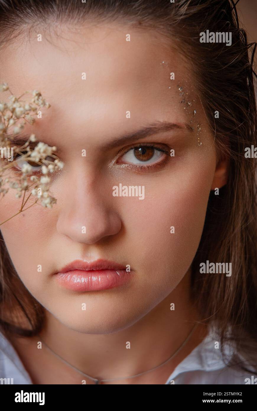 Elegante ritratto di una donna con dettagli floreali e trucco glitter. Donna caucasica con glitter sul viso. Sfondo beige. Foto Stock