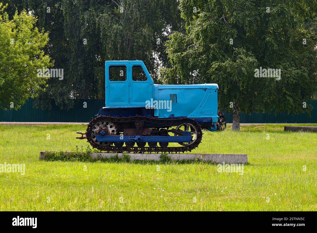 un vecchio trattore blu tracciato sullo sfondo di una foresta e di un campo verdi. Foto Stock