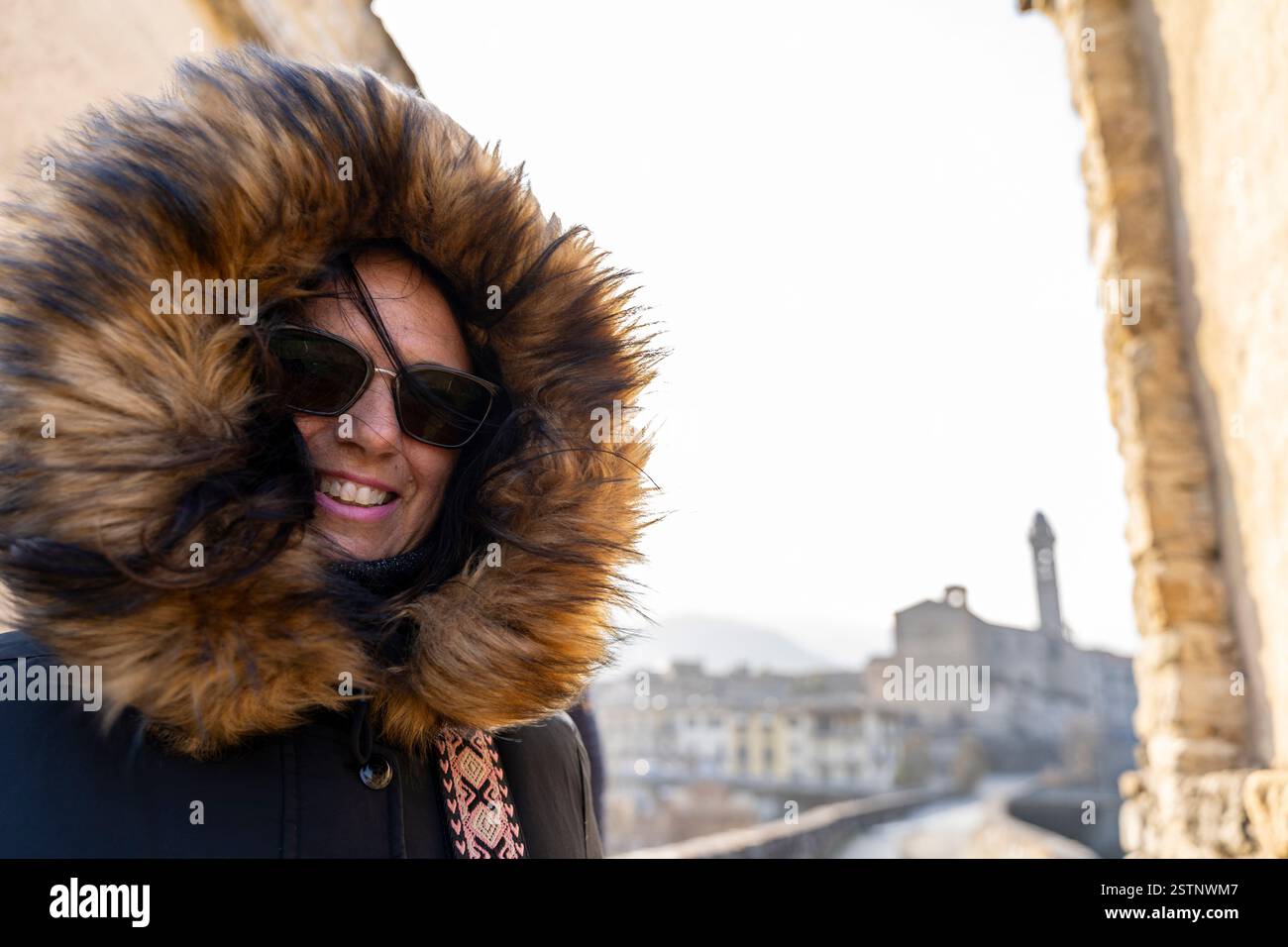 bella donna di mezza età con abiti invernali e occhiali da sole che si fa un selfie di fronte a un villaggio storico Foto Stock