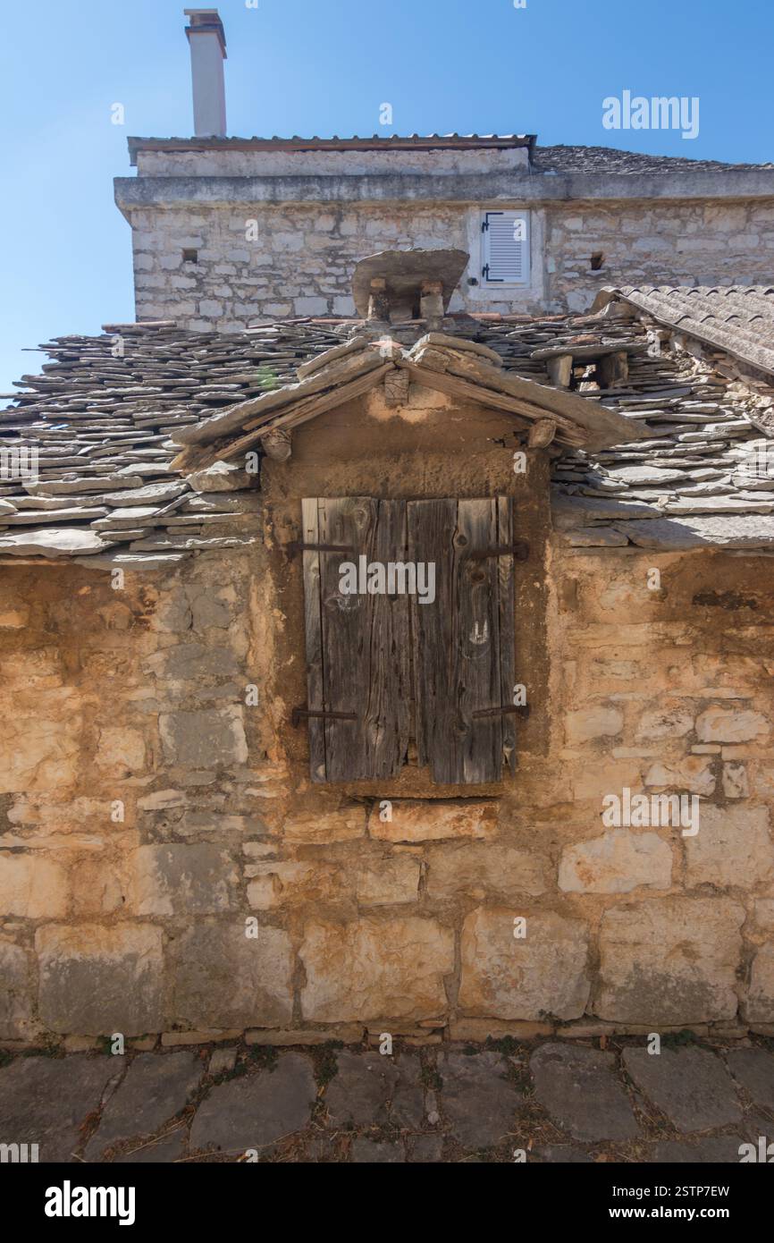 Incantevole vista di un rustico edificio in pietra caratterizzato da persiane in legno intemperie e da un tetto in ardesia, sotto un cielo blu brillante, che evoca un senso di storia e. Foto Stock