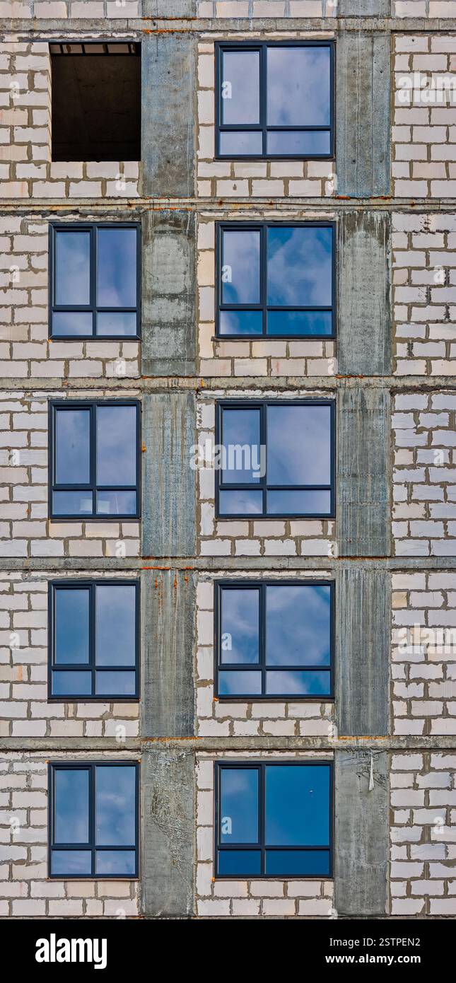 Fila verticale delle finestre dell'edificio di appartamenti in fase di sviluppo con riflessi di cielo blu in vetro Foto Stock