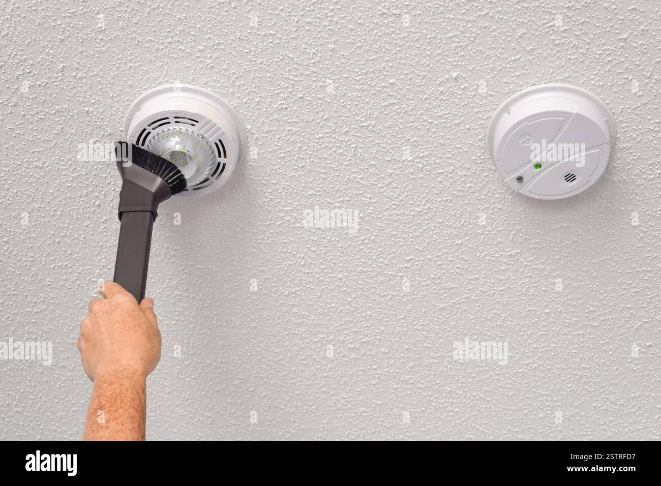 La mano della persona aspira rilevatori di fumo e monossido di carbonio sul soffitto di una stanza domestica Foto Stock
