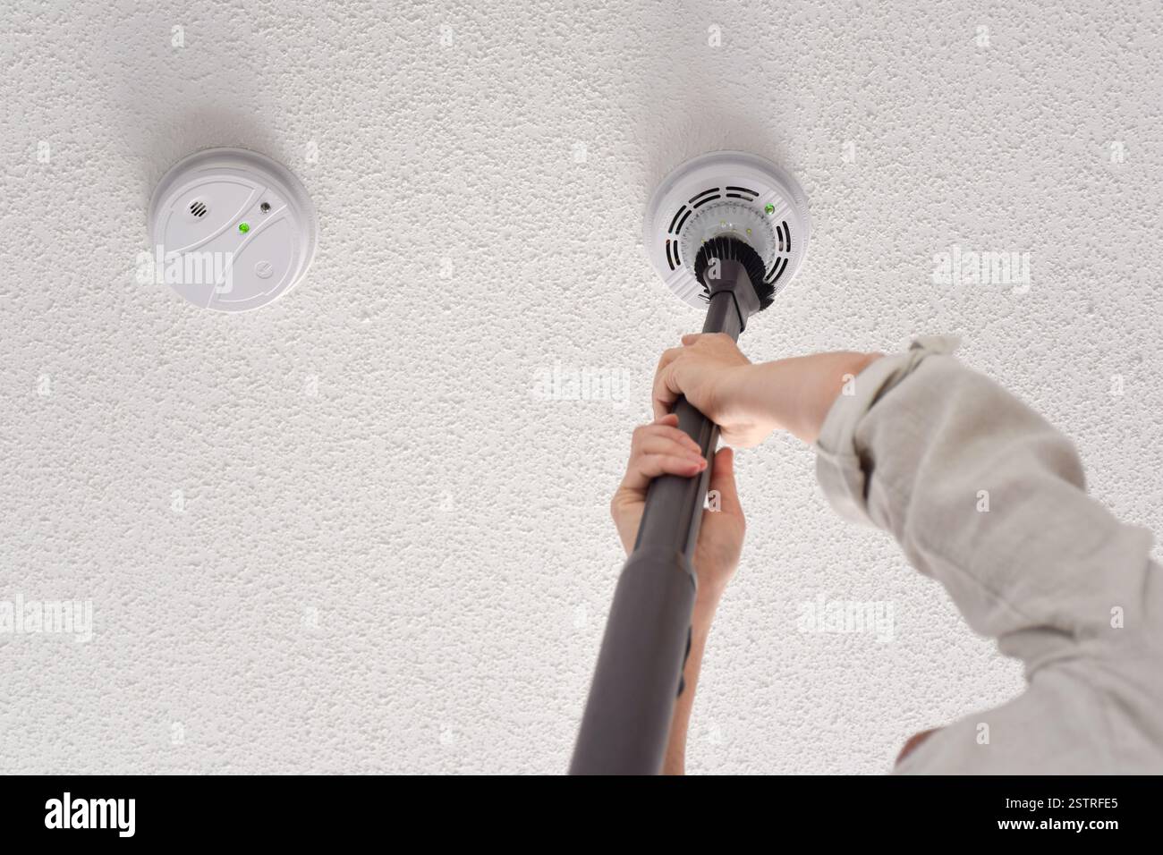 Donna che aspira rilevatori di fumo e monossido di carbonio su un soffitto di una stanza domestica con spazio di copia Foto Stock