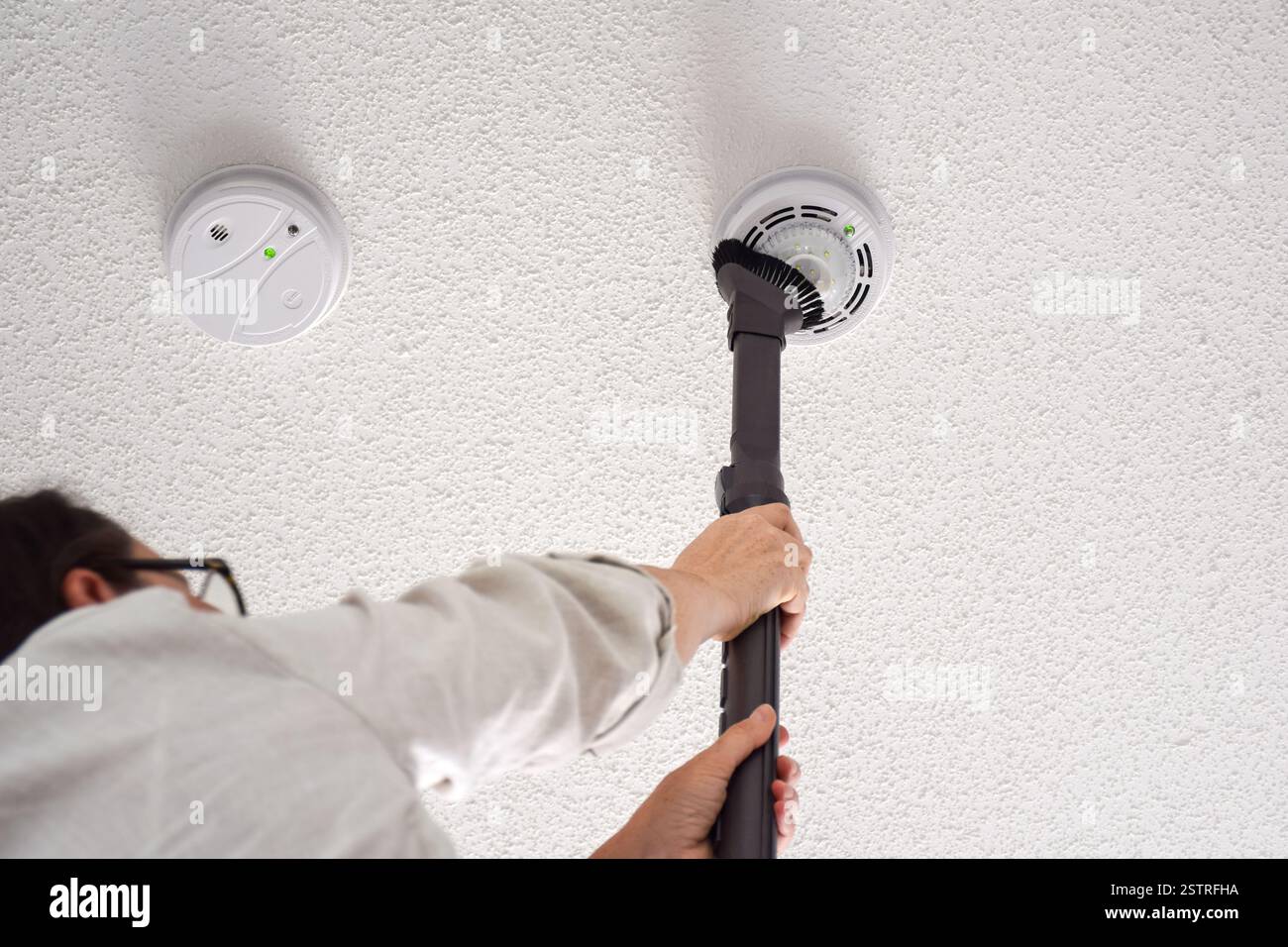 Donna che aspira rilevatori di fumo e monossido di carbonio su un soffitto di una stanza domestica Foto Stock