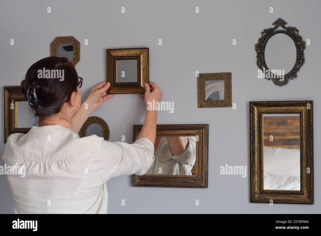 La donna sta appendendo uno specchio come parte di un muro della galleria Foto Stock
