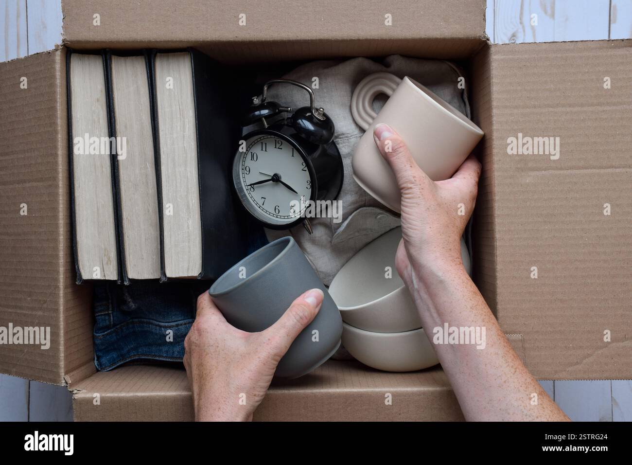 Mani di una persona che colloca oggetti personali usati in una scatola di cartone, donazioni, paracadute o concetto di movimento Foto Stock