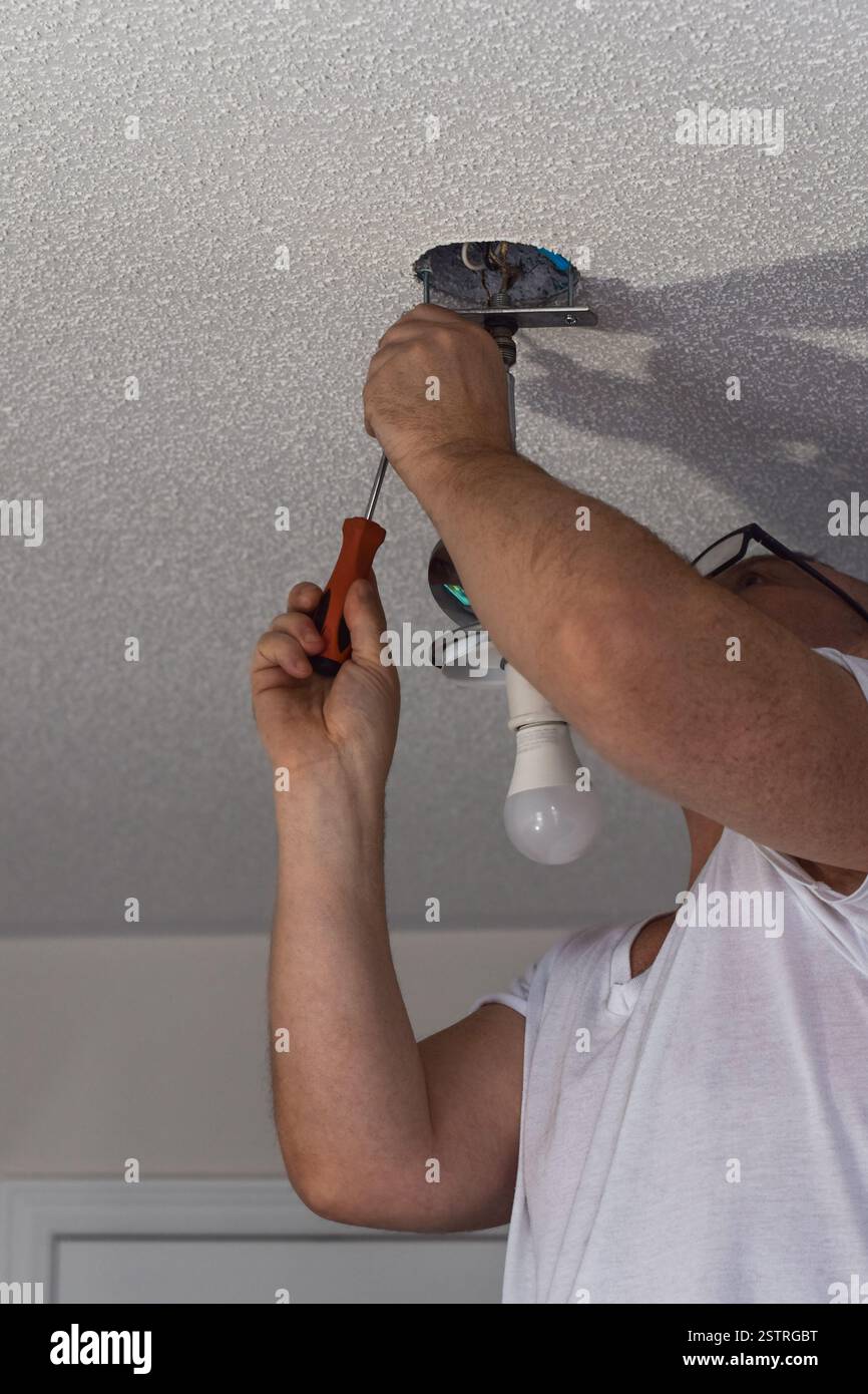 L'uomo di mezza età sta sostituendo la lampada da soffitto con un cacciavite Foto Stock