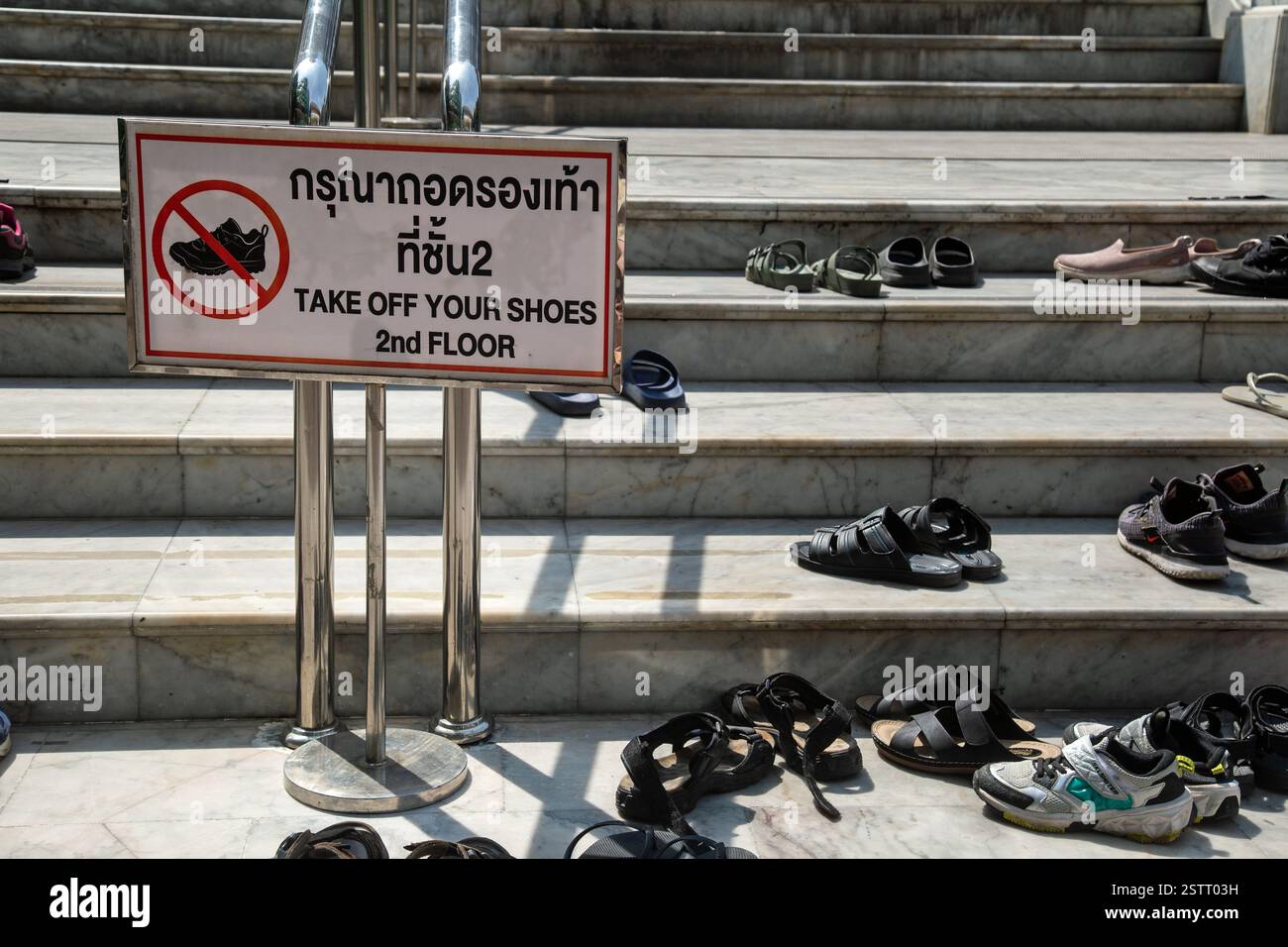 Bangkok, Thailandia, gennaio 2025, scalini per un tempio buddista coperto di scarpe da un cartello che richiede ai visitatori di rimuovere le scarpe. Foto Stock