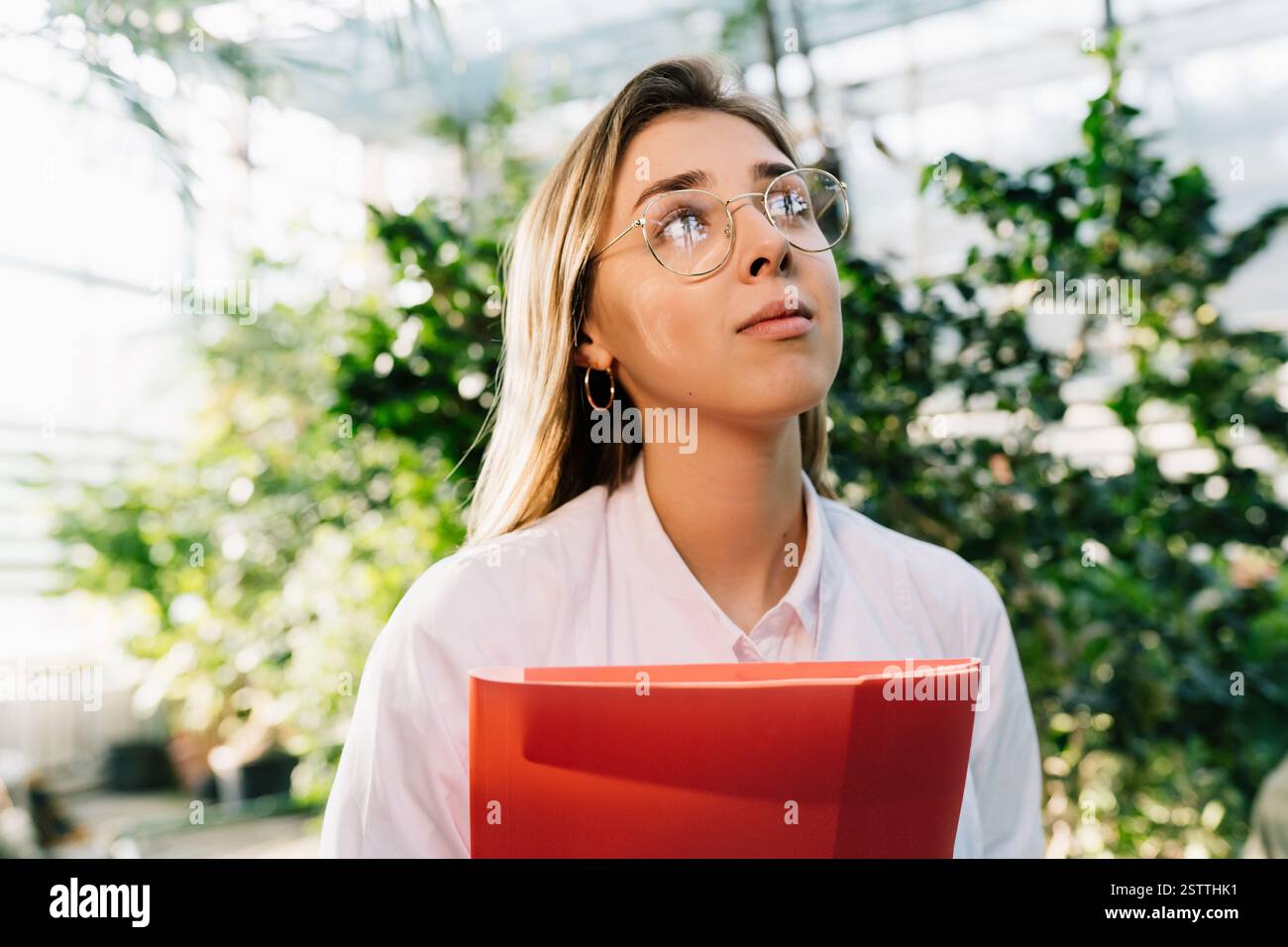 Giovane ingegnere agricolo che lavora in serra. Giovane scienziata femminile guarda via Foto Stock