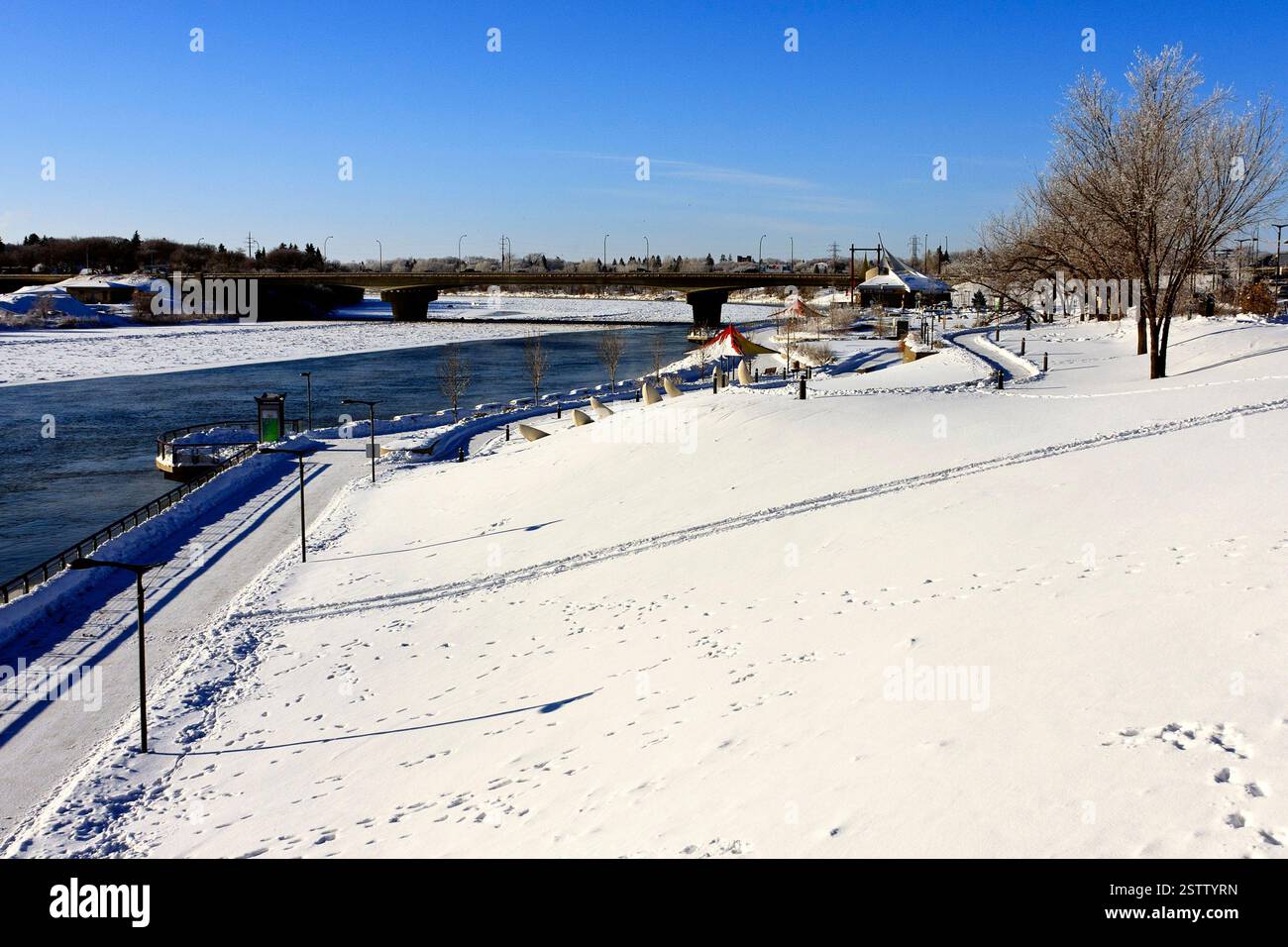 Paesaggio innevato con un fiume e un ponte sullo sfondo. La neve copre il terreno e gli alberi Foto Stock